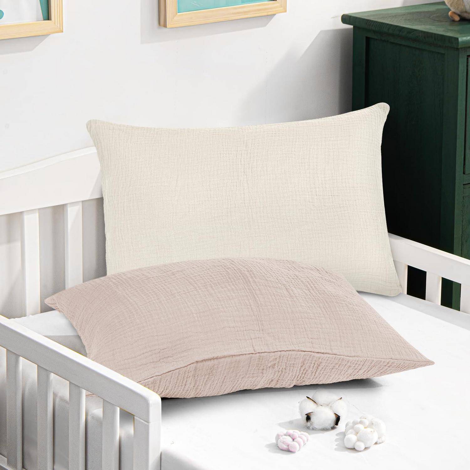 Weißes Babybett mit cremefarbenen und beigen Kissen sowie kleinen Baby-Rasseln auf der Matratze in einem zimmerähnlichen Kinderzimmer.