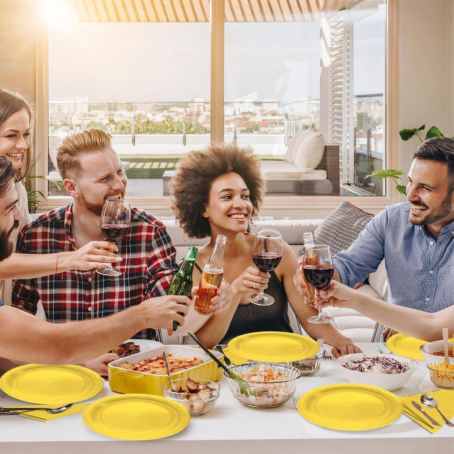 Gruppe von Freunden, die mit Weingläsern um einen Terrassenesstisch herum lächeln und anstoßen, der mit Essen und gelben Tellern bei einer ungezwungenen Zusammenkunft gedeckt ist.