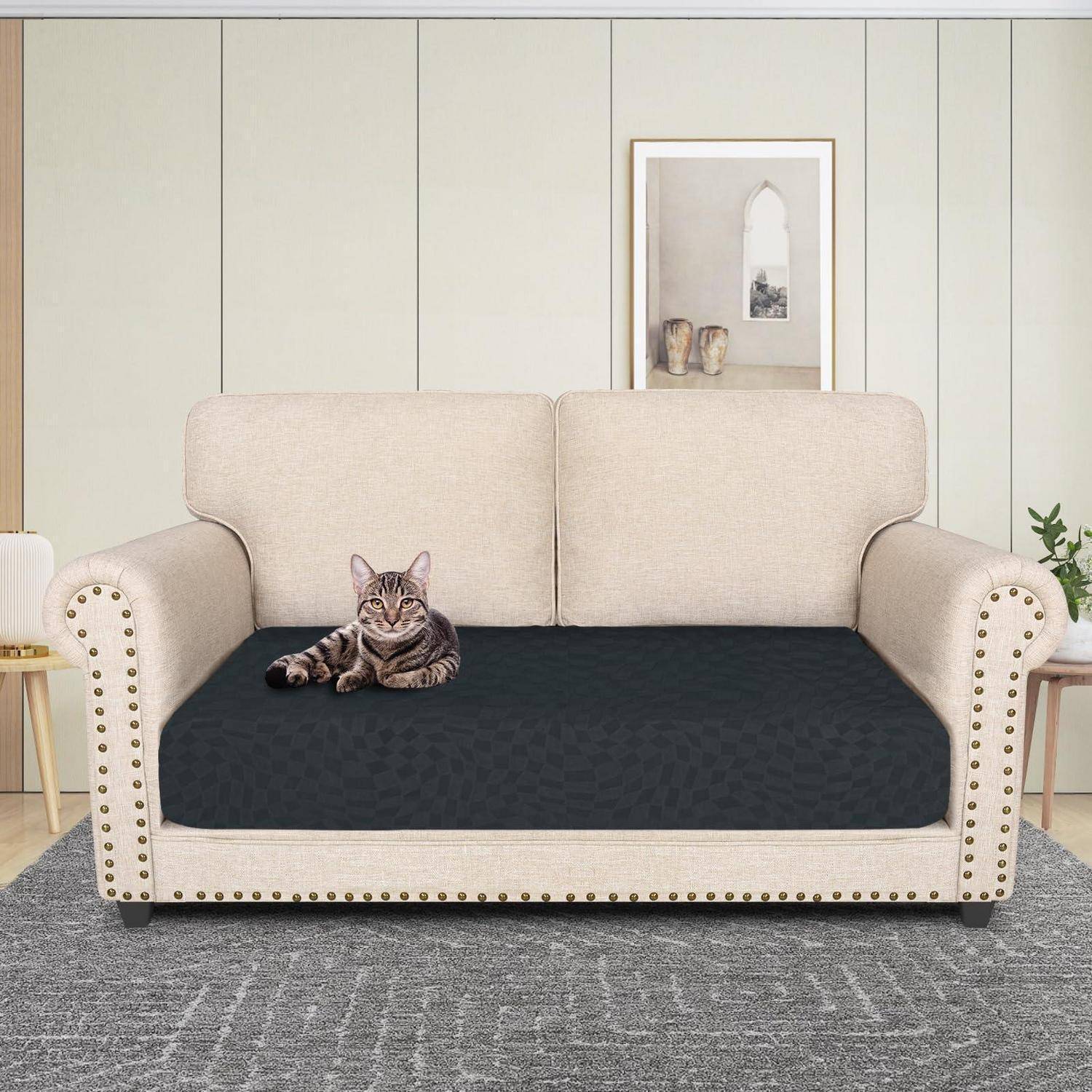 Eine getigerte Katze liegt auf einer dunklen Sitzbezug auf einem beigen Zweisitzer in einem hellen Wohnzimmer.