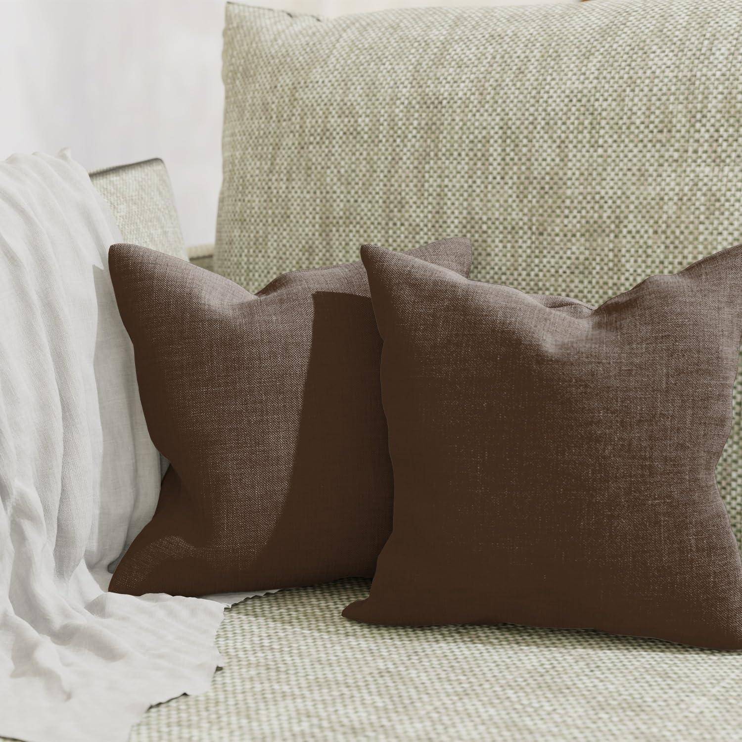 Braun- und cremefarbene Wurf-Kissen auf einem strukturierten beigen Sofa mit einer drapierten weißen Decke, das eine gemütliche Wohnzimmer-Sitzanordnung zeigt.
