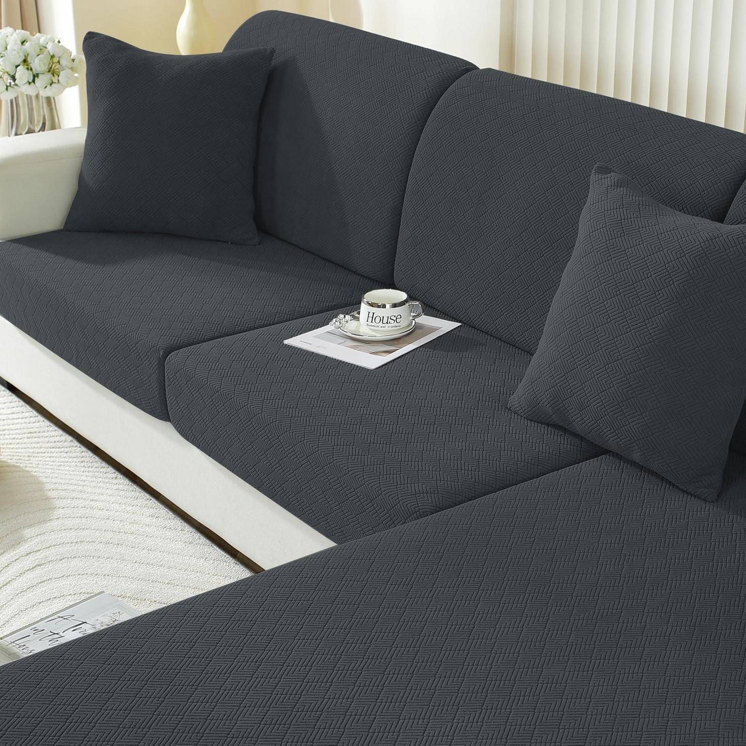 Dunkelgraues Ecksofa mit zwei Kissen und einer Tasse auf einem Magazin in einem hellen Wohnzimmer.