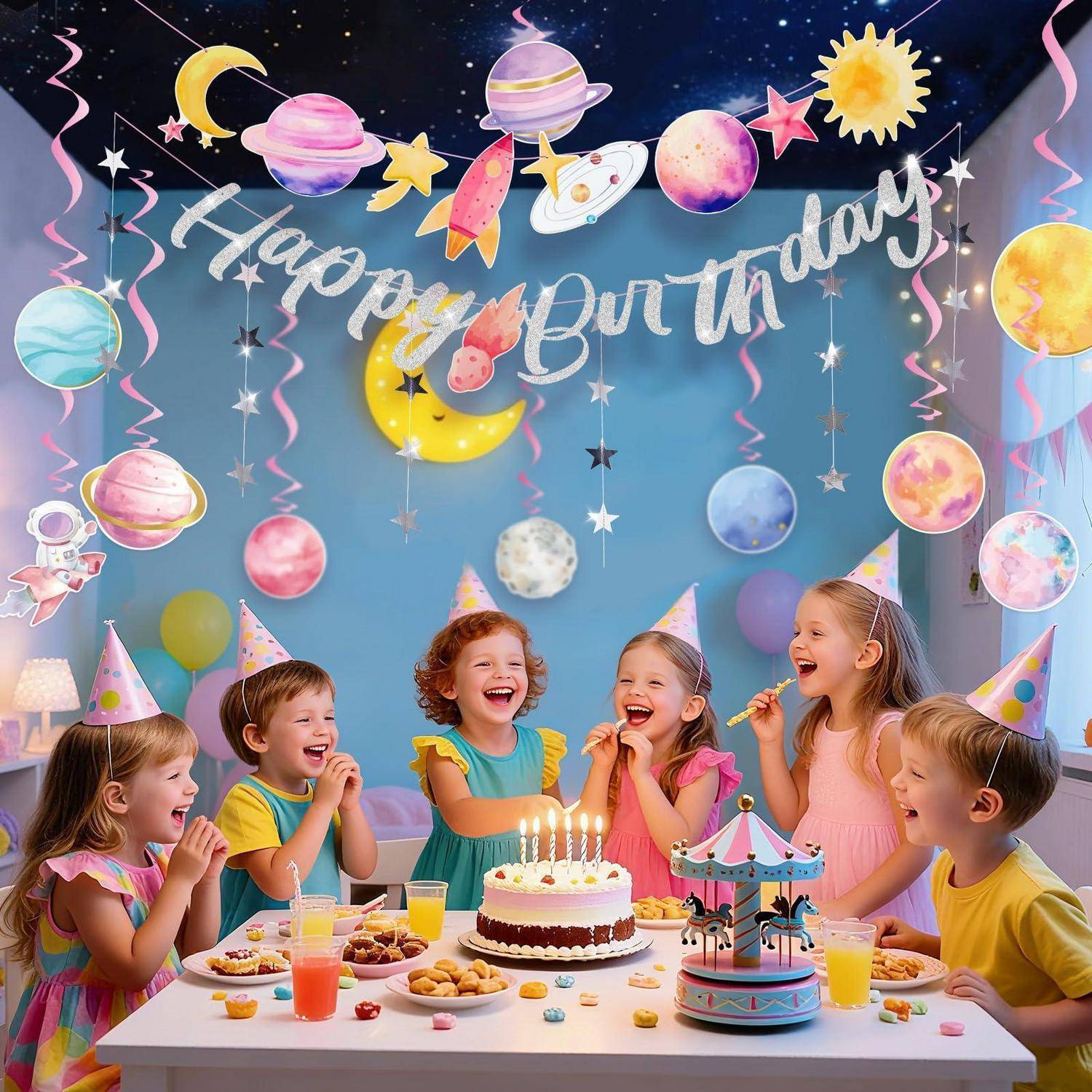 Kinder in Partyhüten feiern einen Geburtstag um einen Kuchen mit brennenden Kerzen herum, vor einem "Happy Birthday""-Hintergrund mit Weltraum-Thema-Dekoration.
