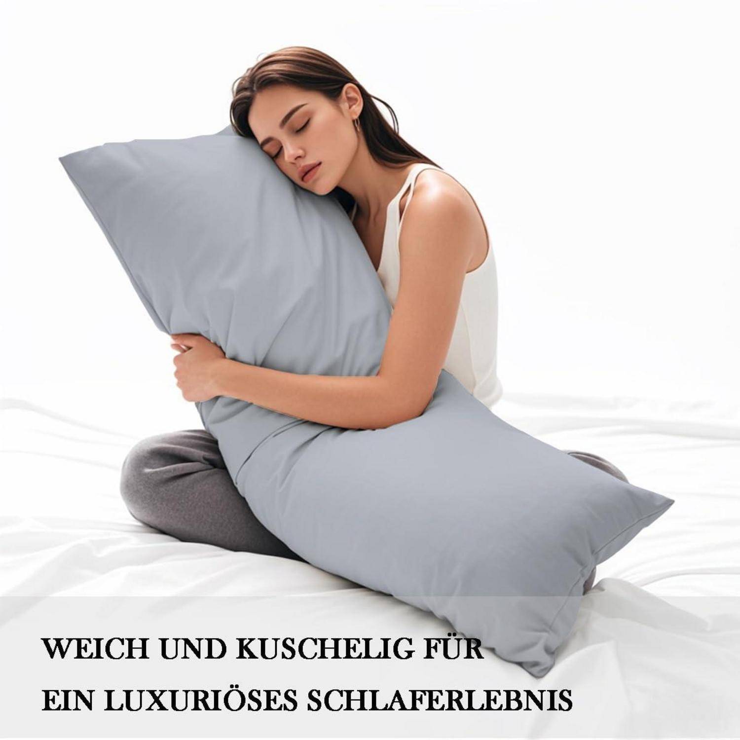 Frau umarmt ein großes graues Körperkissen auf einem Bett, mit deutschem Text: 'WEICH UND KUSCHELIG FÜR EIN LUXURIÖSES SCHLAFERLEBNIS'.