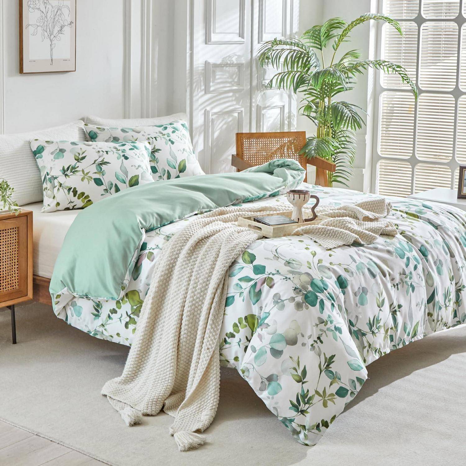 Helles Schlafzimmer mit einem Bett mit Blumenmuster, mintgrüner Decke, strukturiertem Überwurf und einer Topfpflanze neben einem sonnendurchfluteten Fenster.