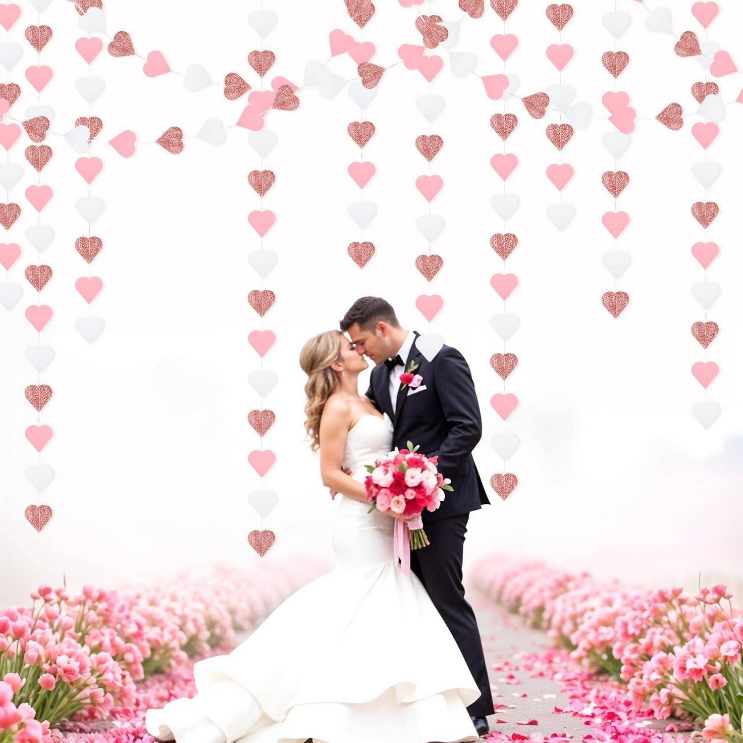 Braut und Bräutigam küssen sich in Hochzeitskleidung unter hängenden rosa und weißen Herzdekorationen und stehen in einem mit Blumen gesäumten Gang.