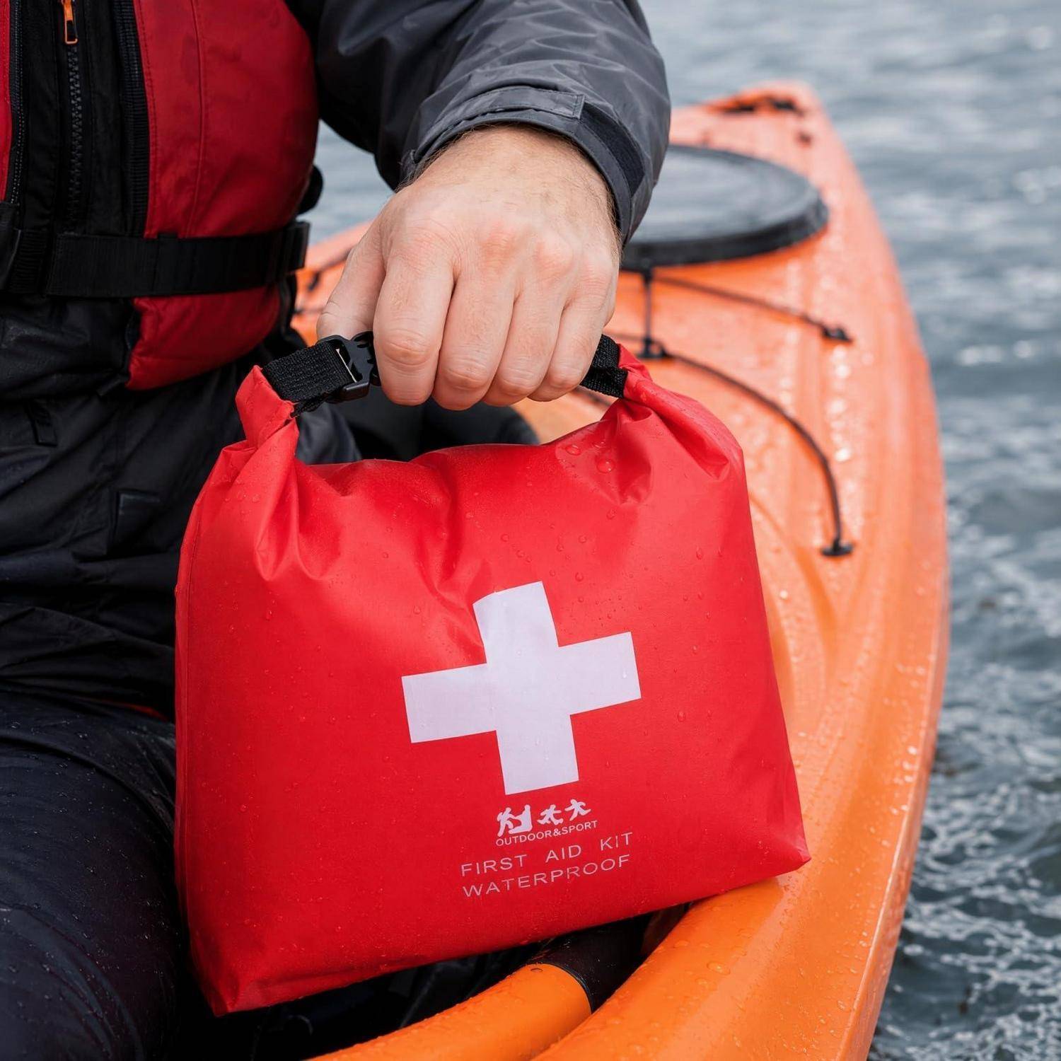 Person in einem orangefarbenen Kajak, der einen roten wasserdichten Erste-Hilfe-Kasten mit einem weißen Kreuz hält.