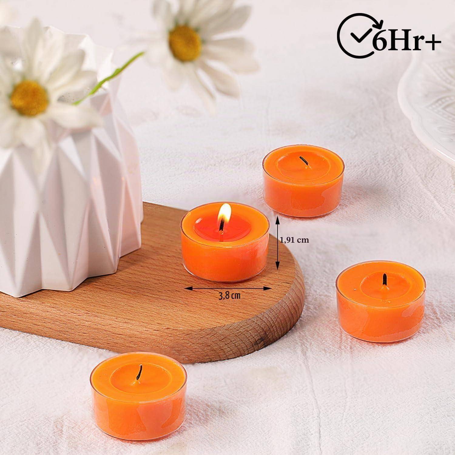 Vier orangefarbene Teelichtkerzen auf einem Holztablett und weißem Tuch; eine ist angezündet, mit „6 Std.+" Brenndauer und Größenetikett 3,8 cm und 1,91 cm.