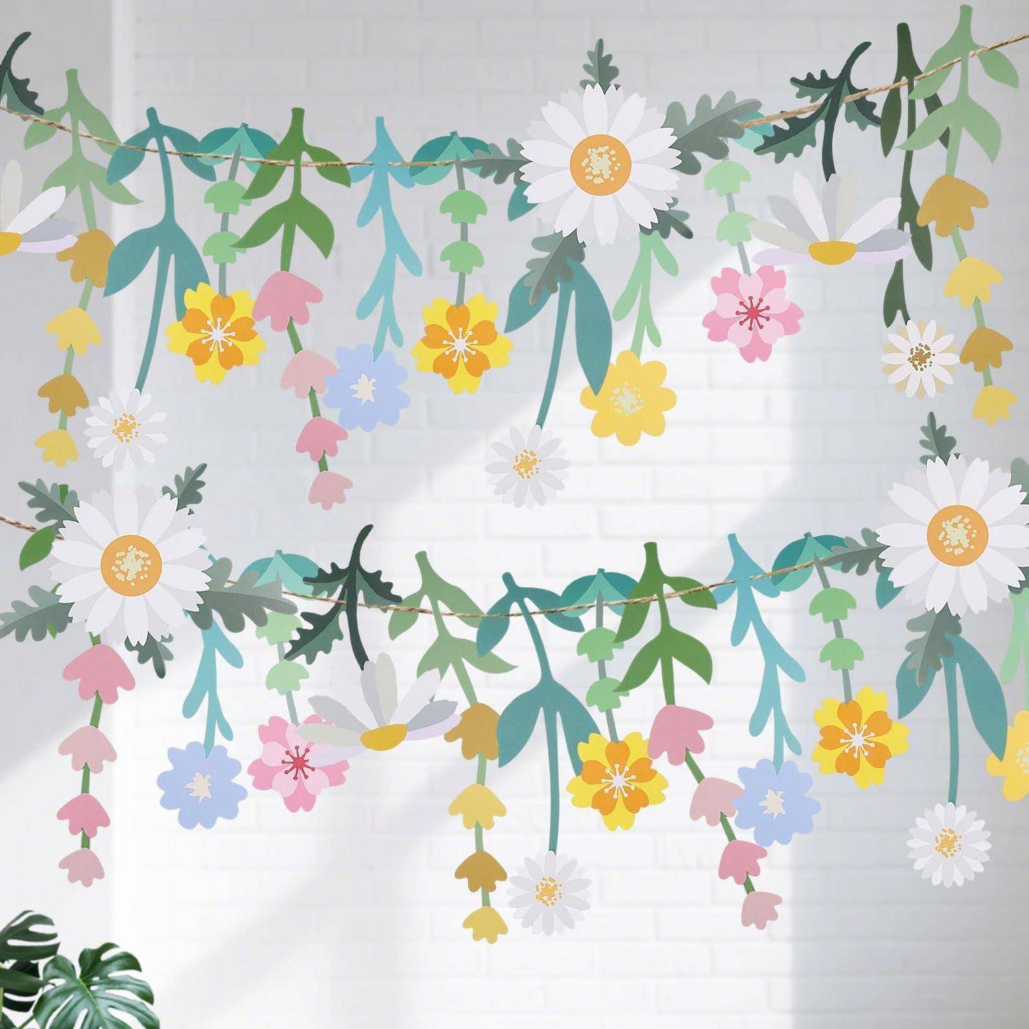 Dekorative Papiergirlanden aus bunten Blüten und Blättern hängen in Schwüngen an einer weißen Backsteinwand.