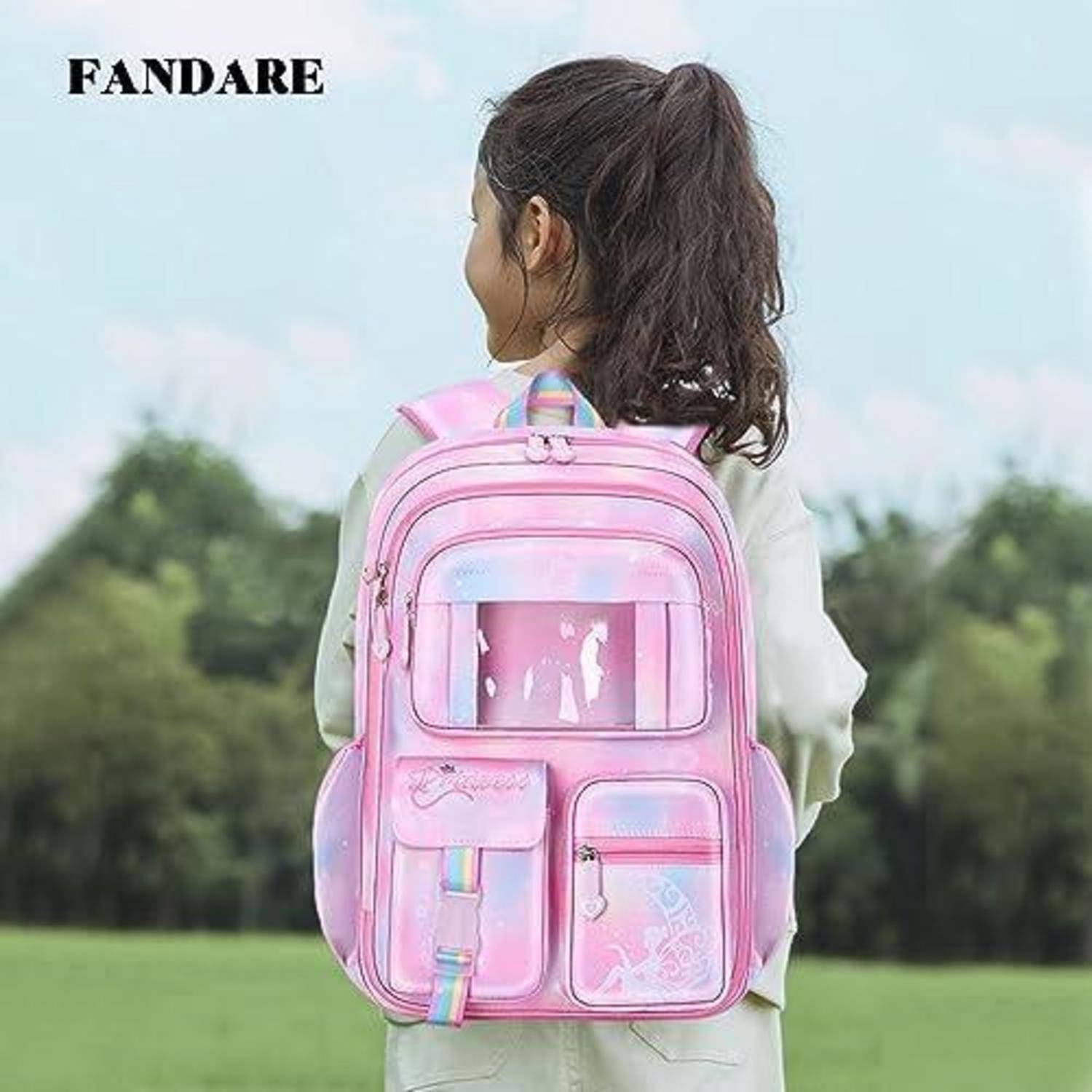 Junges Mädchen von hinten zu sehen, das einen glänzenden rosa Rucksack mit mehreren vorderen Taschen trägt, steht im Freien auf einer Wiese.