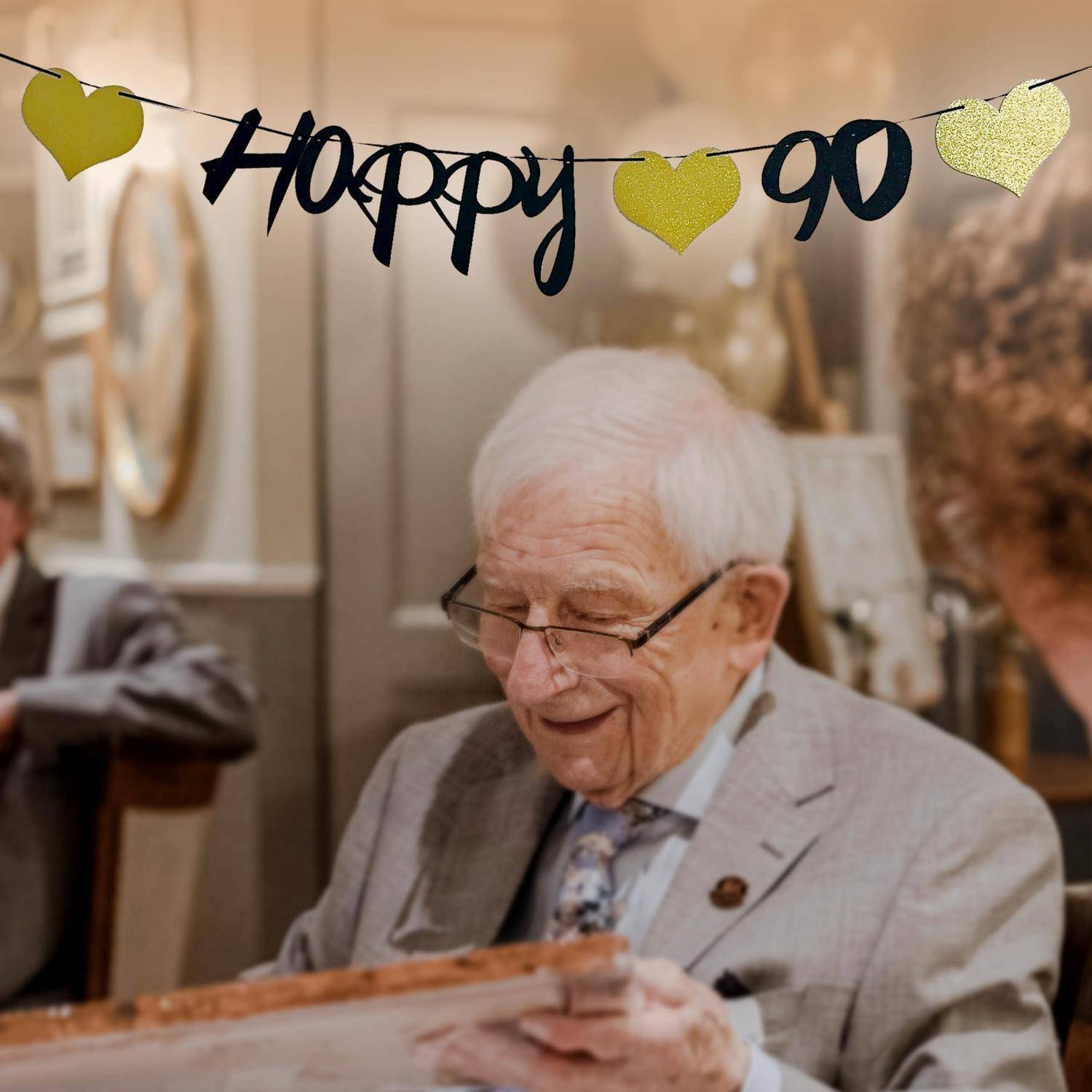 Ein älterer Mann im Anzug lächelt unter einem „Happy 90