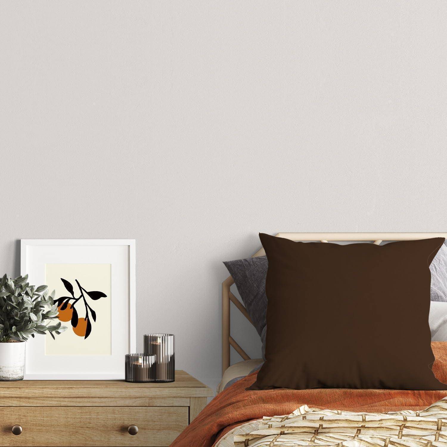 Minimalistisches Schlafzimmer mit ordentlich gemachtem Bett, braunem Akzentkissen, gerahmtem Obstdruck, Pflanze, Kerze und hölzernem Nachttisch-Kommode.