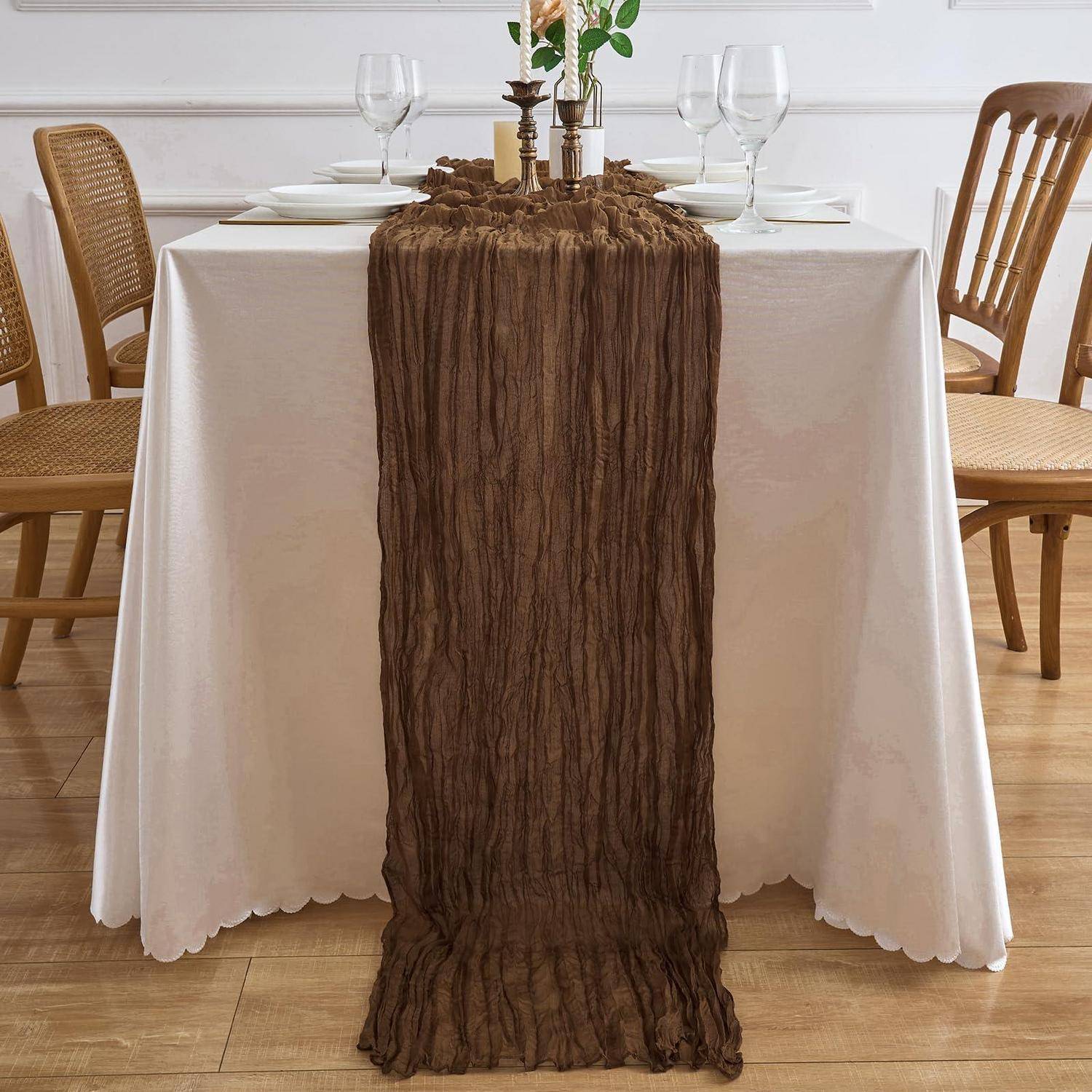 Esstisch für ein formales Essen eingedeckt, mit weißem Tischtuch, braun strukturiertem Tischläufer, Gedeck, Gläsern und Holzstühlen.