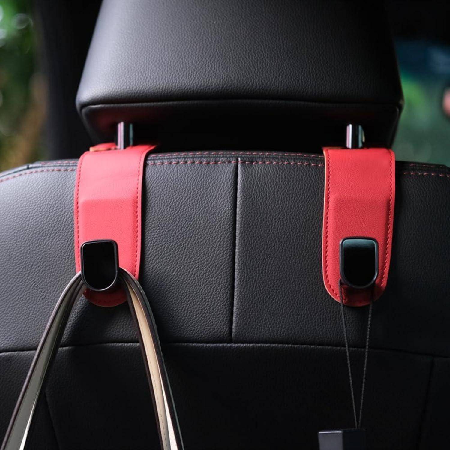 Nahaufnahme einer Kopfstütze eines Autositzes mit zwei roten Riemenhaken, die einen schwarzen Griffeiner Tasche an Ort und Stelle halten.