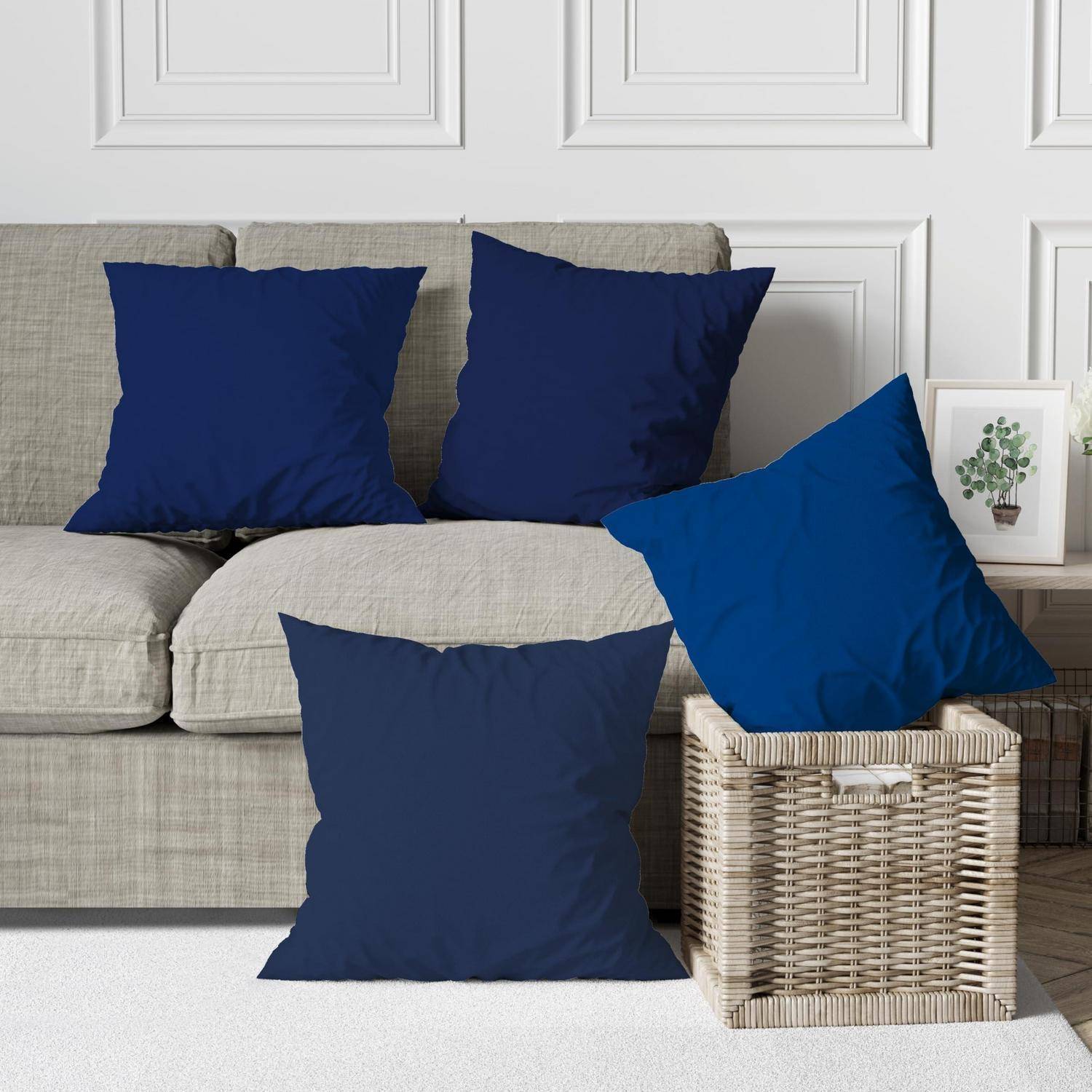 Vier blaue quadratische Wurfsotakissen auf einem beigen Sofa und Korbkorb in einem Wohnzimmer, vor einer weiß getäfelten Wand.