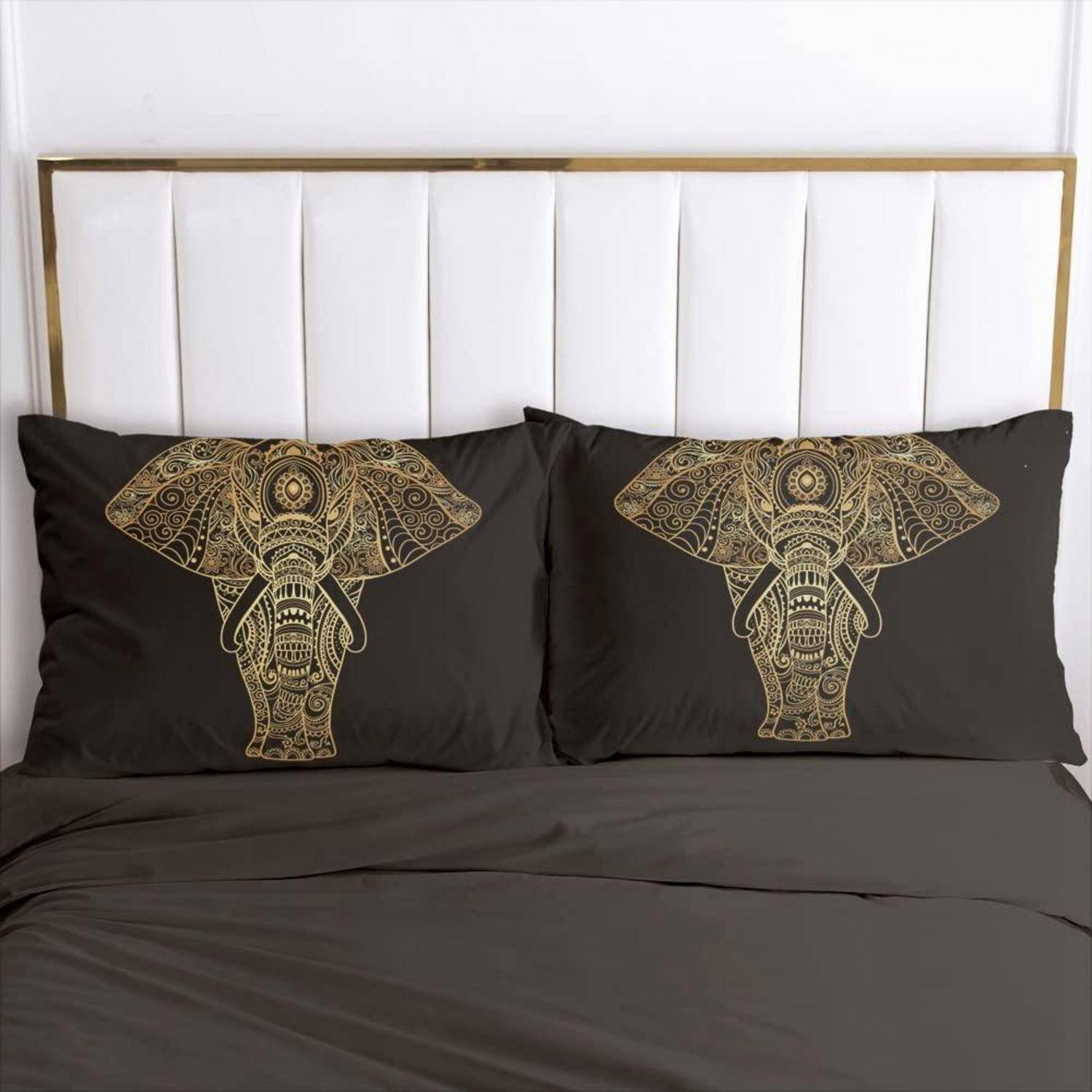 Ein Bett mit dunkler Bettwäsche und zwei schwarzen Kissen mit goldenen Elefantenkopf-Designs vor einem weiß gepolsterten Kopfteil.
