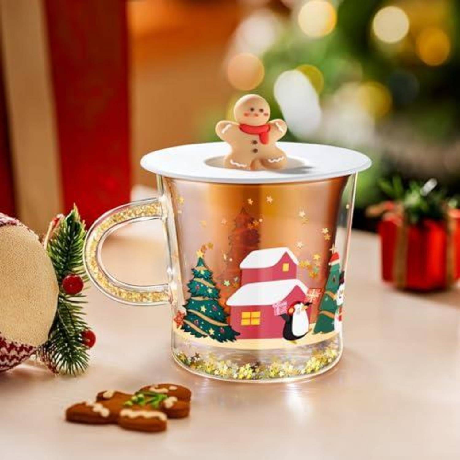 Weihnachtsthematische Glastasse mit goldenem Innenbereich und festlichem Haus- und Baumdesign, gekrönt durch eine Lebkuchenmann-Deckel-Verzierung.