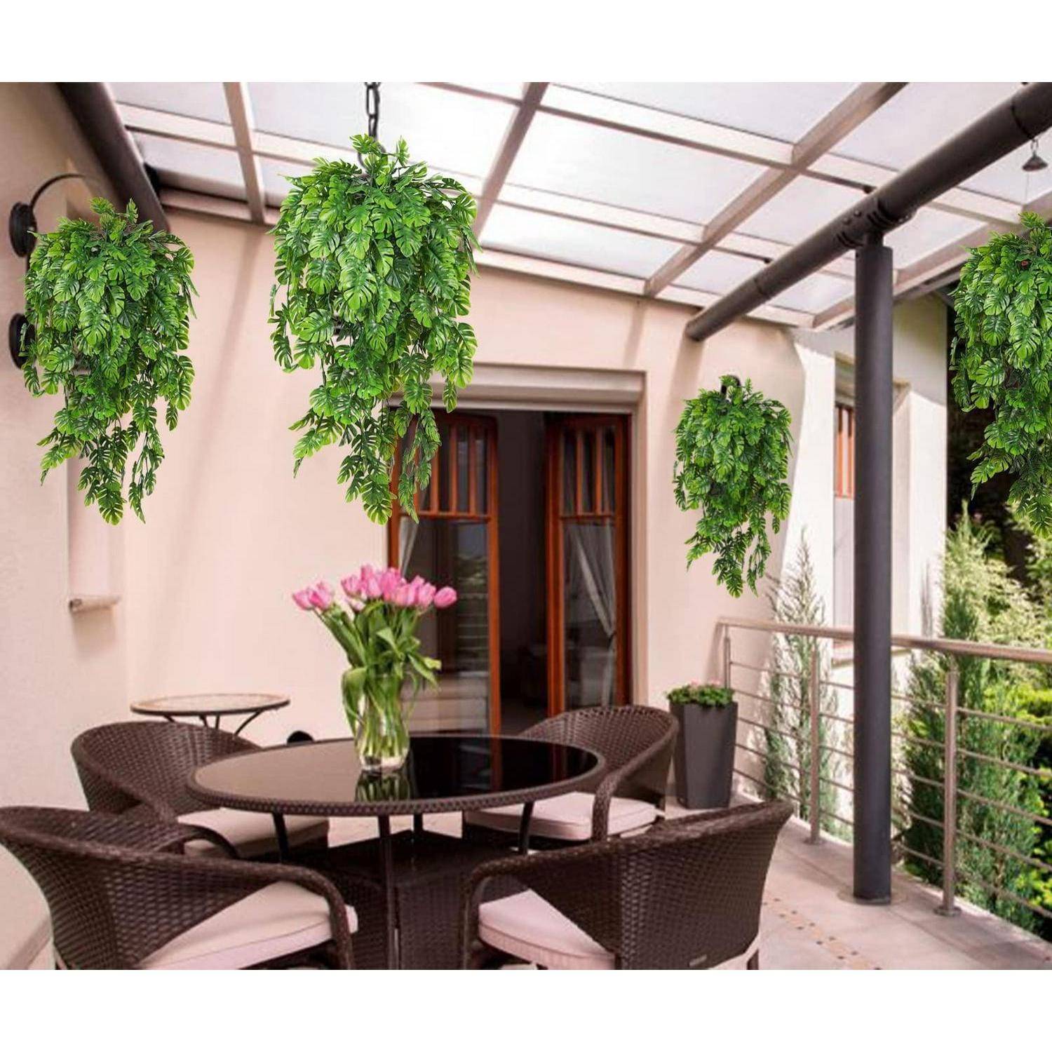 Überdachte Terrasse mit Korbstühlen und einem runden Tisch, umrahmt von hängenden grünen Pflanzen und einer Vase mit rosa Blumen, neben einer Schiebetür.
