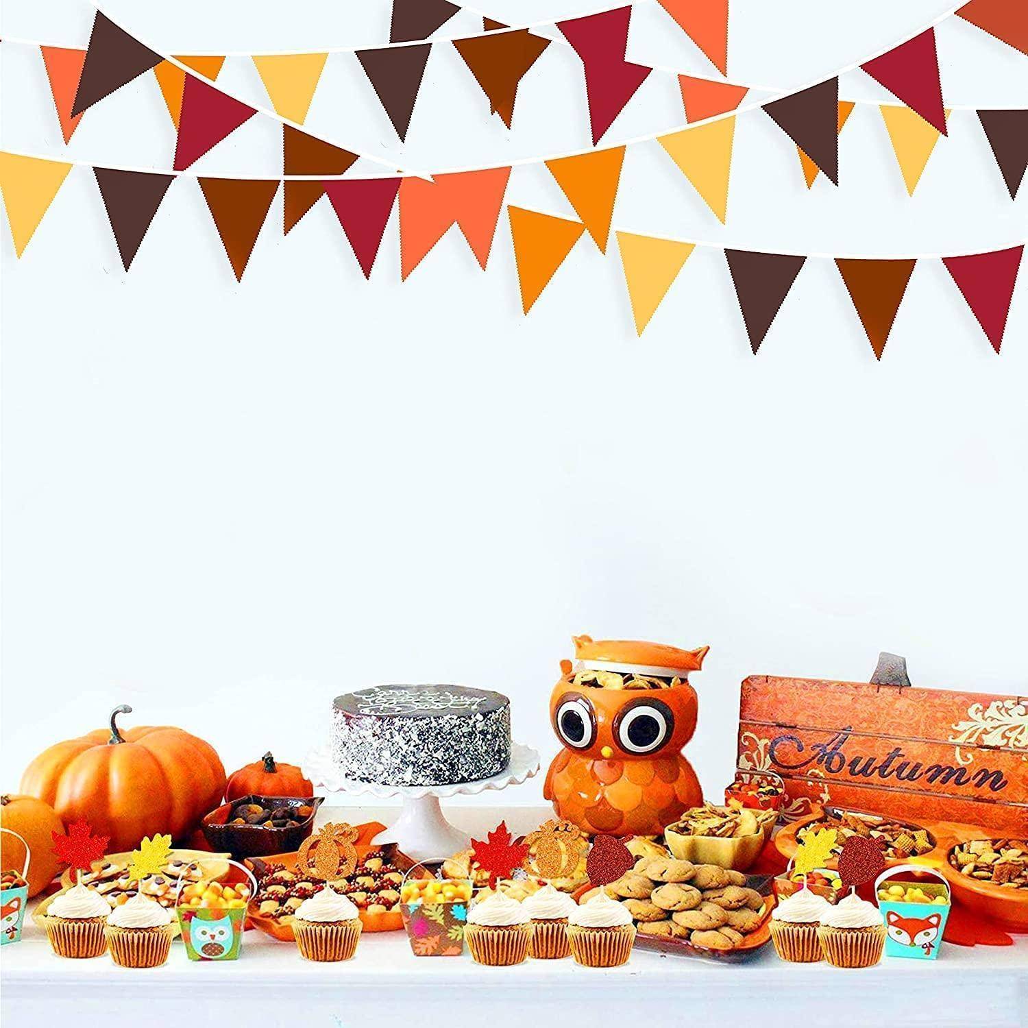 Herbst-Nachtischtisch mit Cupcakes, Keksen, Kürbissen und einer Eulendekoration unter bunter Herbstgirlande.