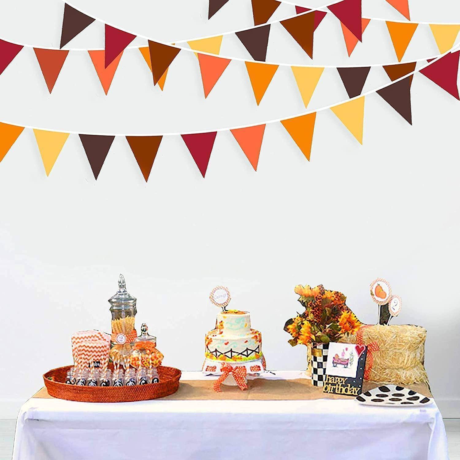 Geburtstagsdesserttisch mit einem Kuchen, Cupcakes, Blumen und Partyzubehör unter orange-, braun- und gelbfarbigen Wimpelgirlanden.