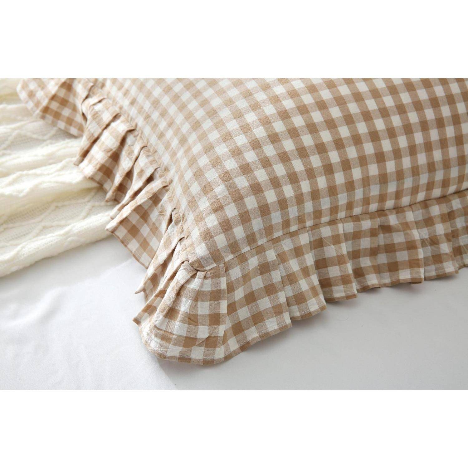 Beige kariertes Kissen mit Rüschenkante auf einem weißen Bett, in Nahaufnahme gezeigt.
