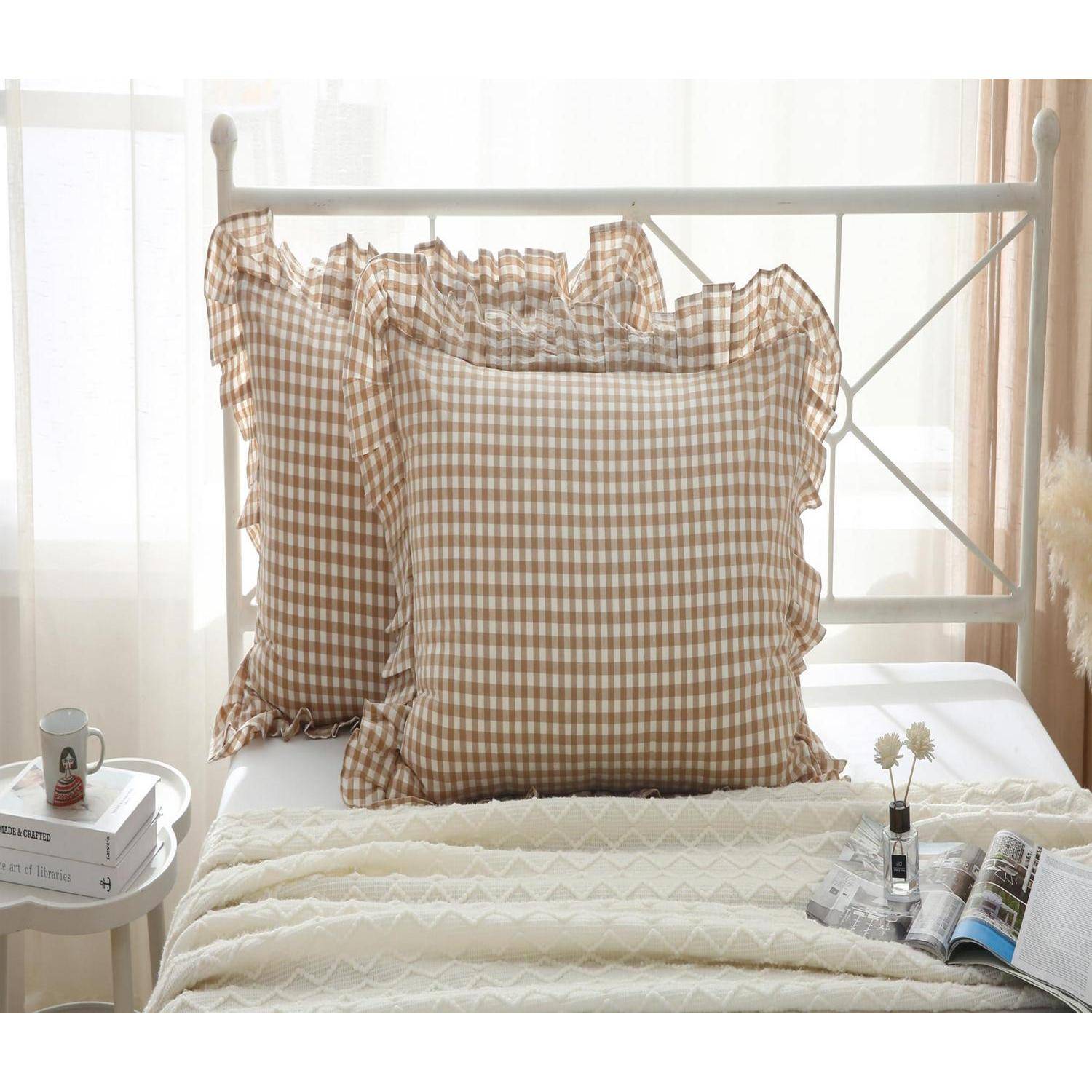 Ein ordentlich gemachtes Bett mit braunen Gingham-Kissen, einer cremefarbenen Steppdecke, einem Nachttisch mit Büchern und einer Tasse sowie einer aufgeschlagenen Zeitschrift.