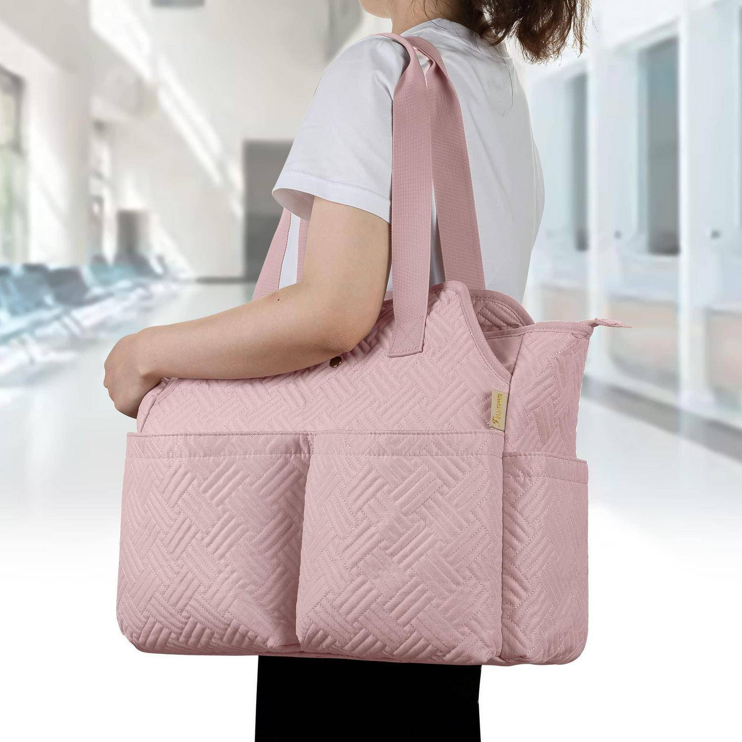 Person, der eine große rosa gesteppte Tragetasche mit Vordertaschen in einem hellen Flur trägt.