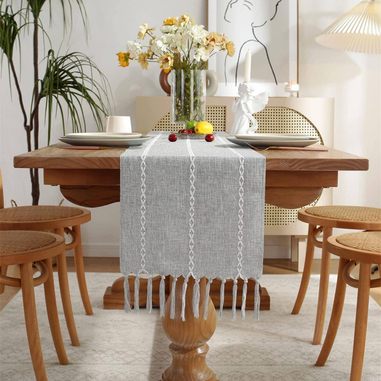 Stilvoller Esstisch mit grauem Tischläufer und einer Vase mit Blumen, umgeben von Holzhockern in einem hellen modernen Raum.