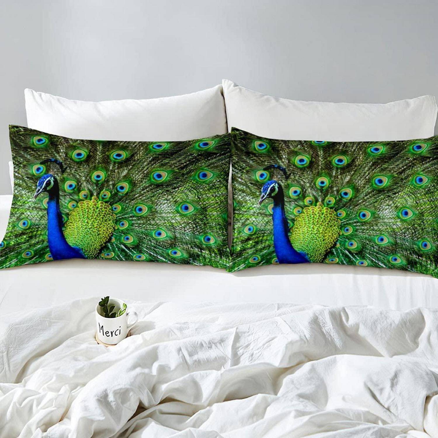 Pfauen-gemusterte Kissenbezüge auf einem ordentlich gemachten weißen Bett mit einem kleinen "Merci""-Blumentopf davor.