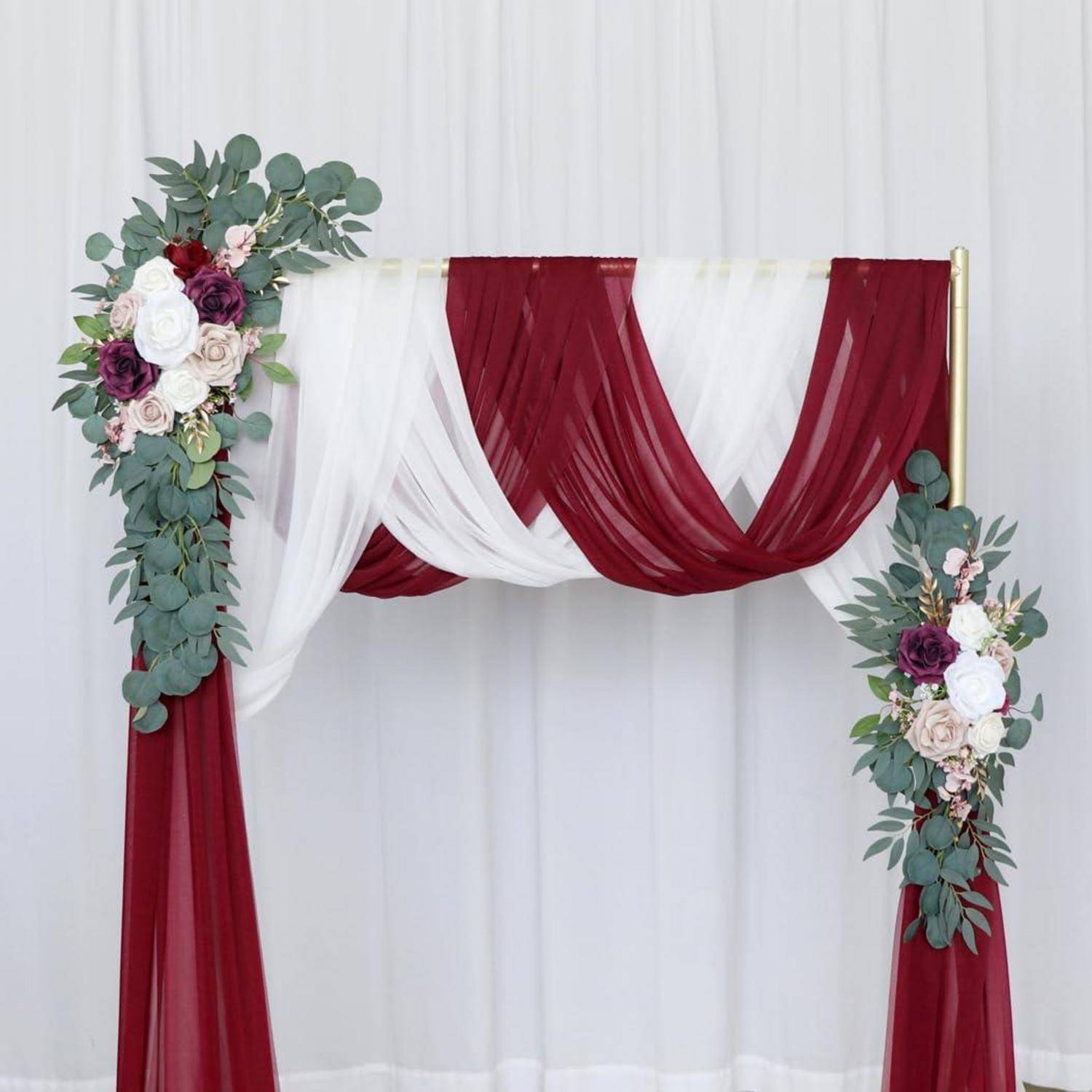 Burgunderrotes und weißes drapiertes Traubogenbogen mit Blumenarrangements auf jeder Seite vor einem weißen Hintergrund.