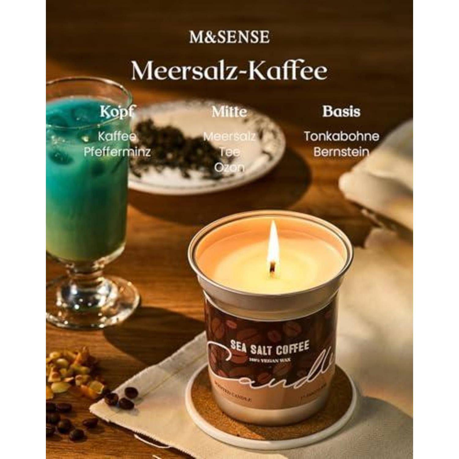 Werbekerze mit der Bezeichnung „Sea Salt Coffee" auf einem Tisch, mit deutschem Text, der die Duftnoten benennt: „Kopf"" Kaffee und Pfefferminze, „Mitte"" Meersalz, Tee, Ozon, „Basis"" Tonkabohne und Amber.