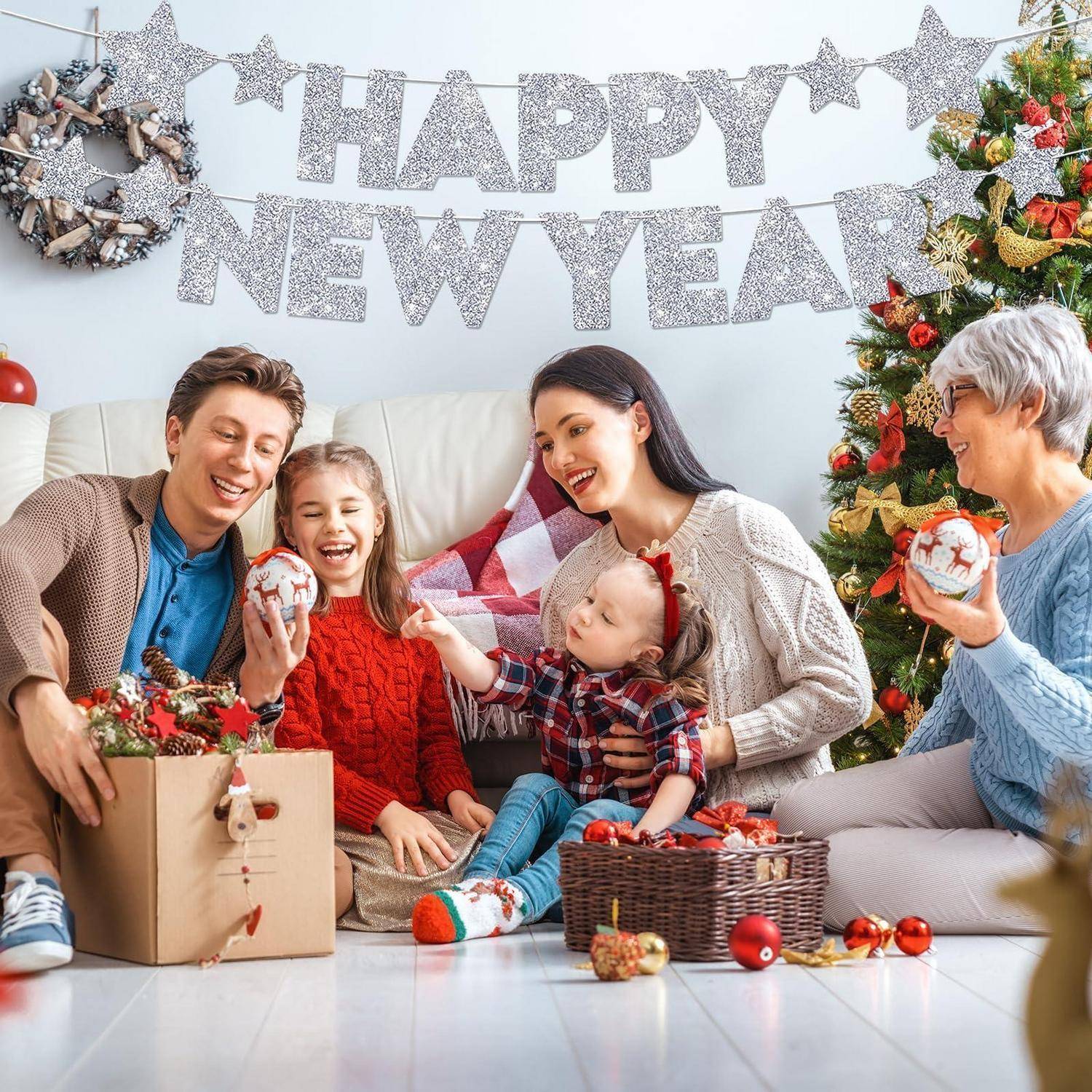 Familie mit vier Personen feiert Neujahr neben einem dekorierten Weihnachtsbaum, lächelt und hält Geschenkornamente unter einem Banner mit der Aufschrift "FROHES NEUES JAHR"".
