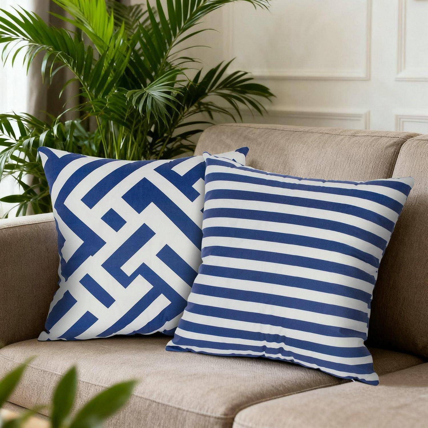 Zwei blau-weiß gemusterte Dekokissen auf einem beigefarbenen Sofa, mit einer grünen Blattpflanze im Hintergrund.