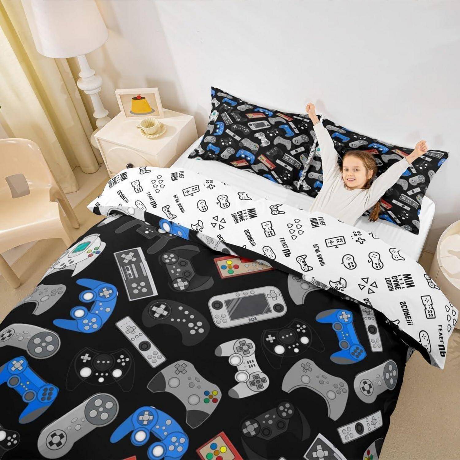 Kind lächelt im Bett unter einer Gaming-Controller-Themen-Bettdecke und Kissen, streckt die Arme nach oben in einem hellen Schlafzimmer.