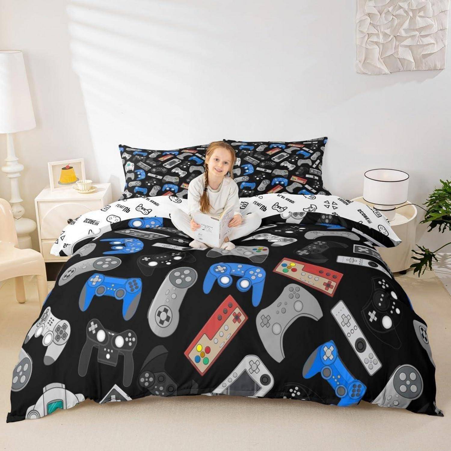 Junges Mädchen, das auf einem Bett mit einer schwarzen Bettdecke und Kissen mit Videospiel-Controller-Muster in einem hellen Schlafzimmer sitzt.
