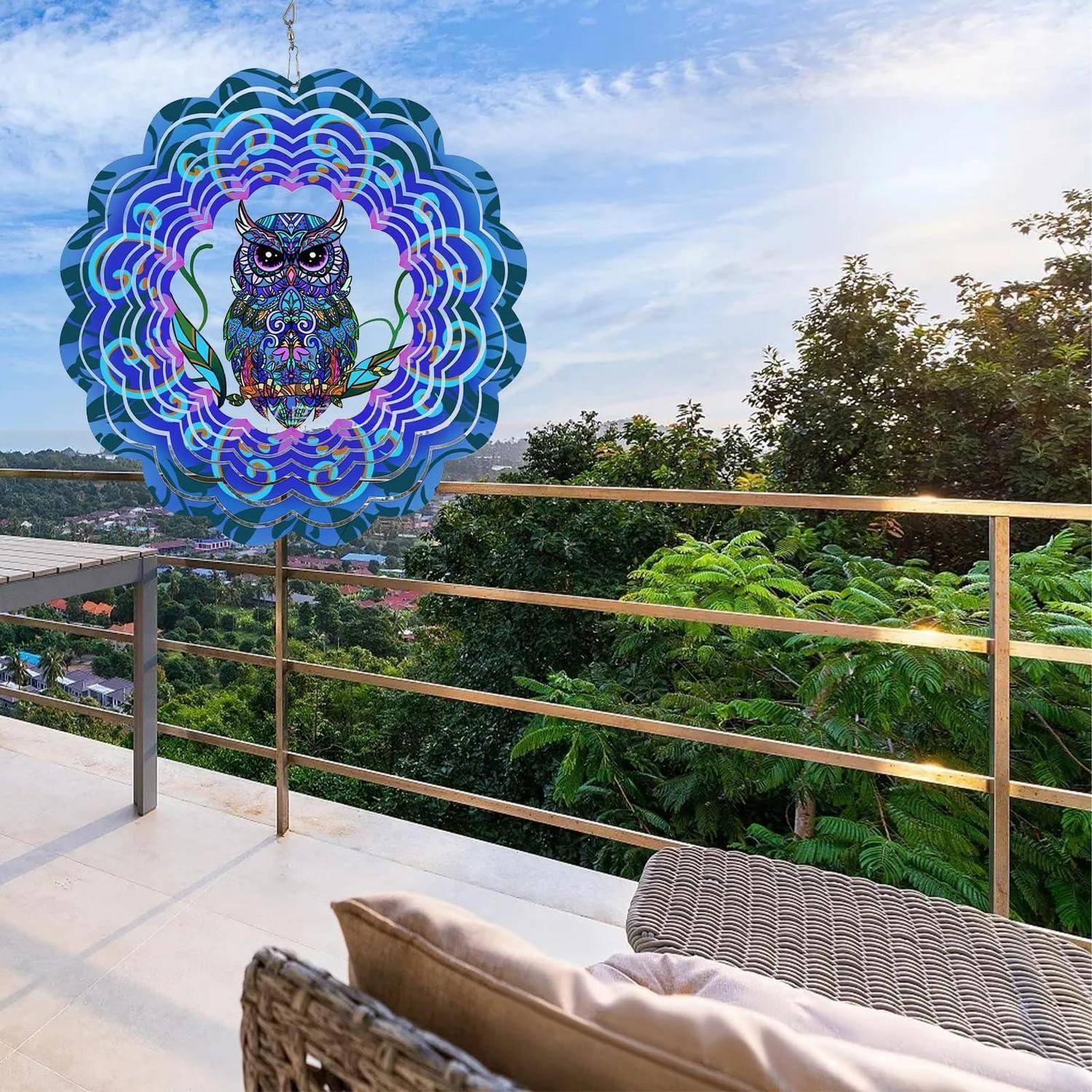 Buntes Eule-Windspiel, das an einem Balkon hängt und auf Bäume und entfernte Dächer bei Sonnenuntergang überblickt.
