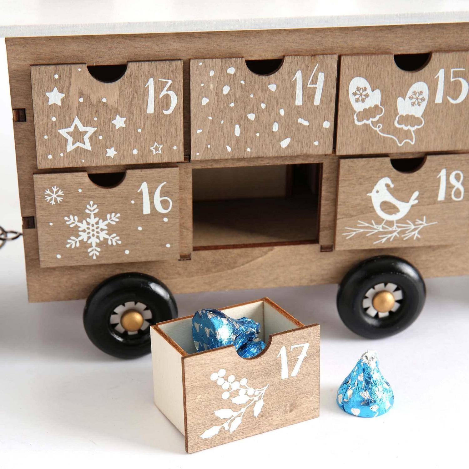 Adventskalender aus Holz mit nummerierten Schubladen 13 bis 18, einige verziert mit Sternen, Schneeflocken, Vögeln und Handschuhen; Schublade 17 ist offen mit blauen Pralinen daneben.