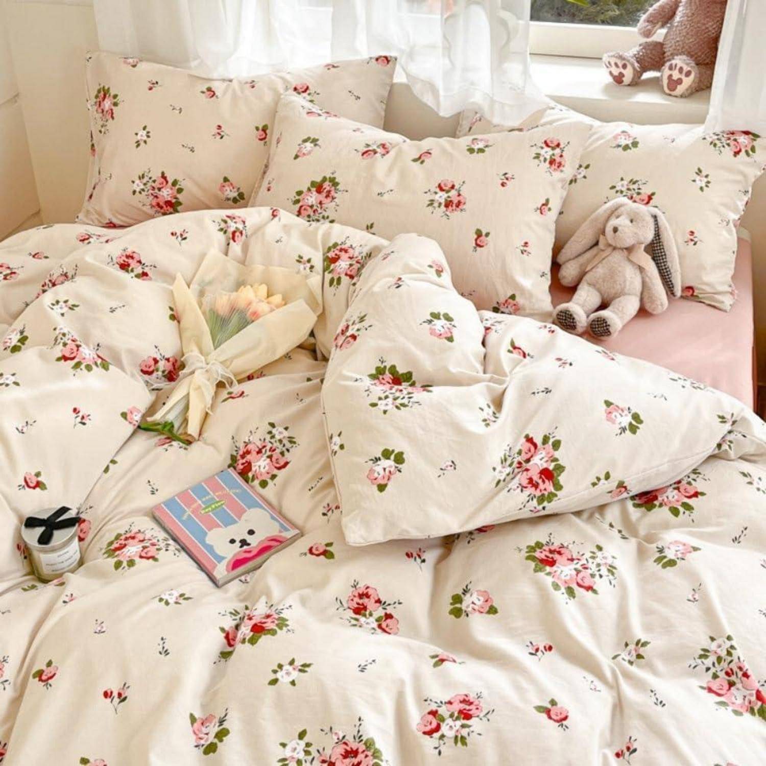 Blumenmuster-Bettwäsche mit Kissen und einer Bettdecke auf einem Bett, mit einem kleinen Teddybär, einem Blumenstrauß und einem Notizbuch in der Nähe des Fensters.
