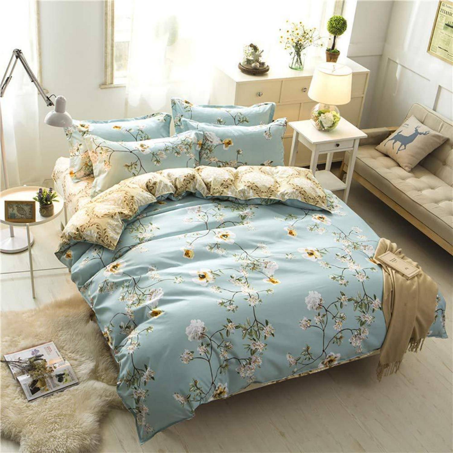 Helles Schlafzimmer mit einem hellblauen Blumenbettset auf einem ordentlich gemachten Bett, umgeben von weißen Möbeln, Lampen und weicher Dekoration.
