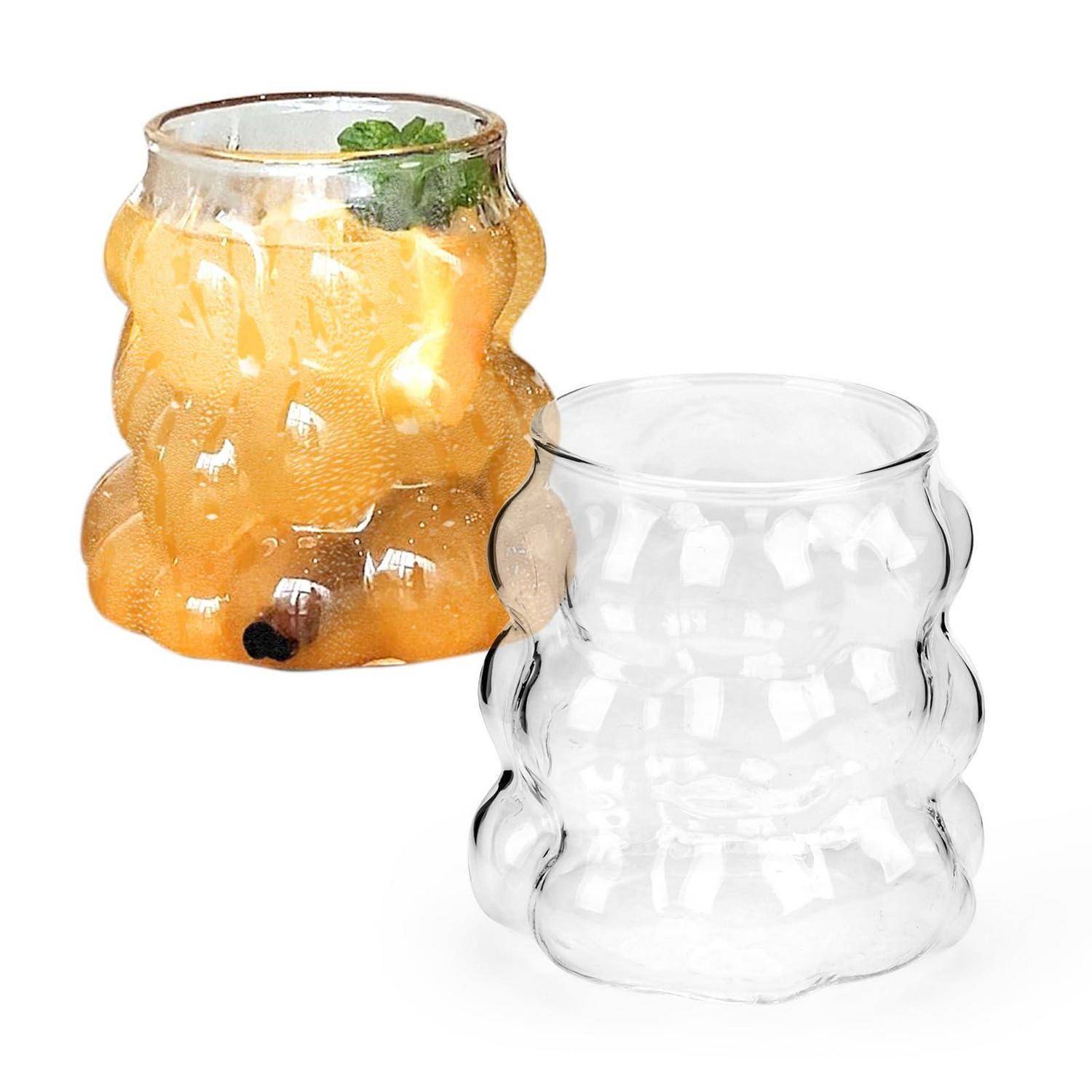 Zwei gewellte Glastassen, eine klar und eine gefüllt mit orangefarbenem Getränk und Eis mit einer Minzgarnitur.