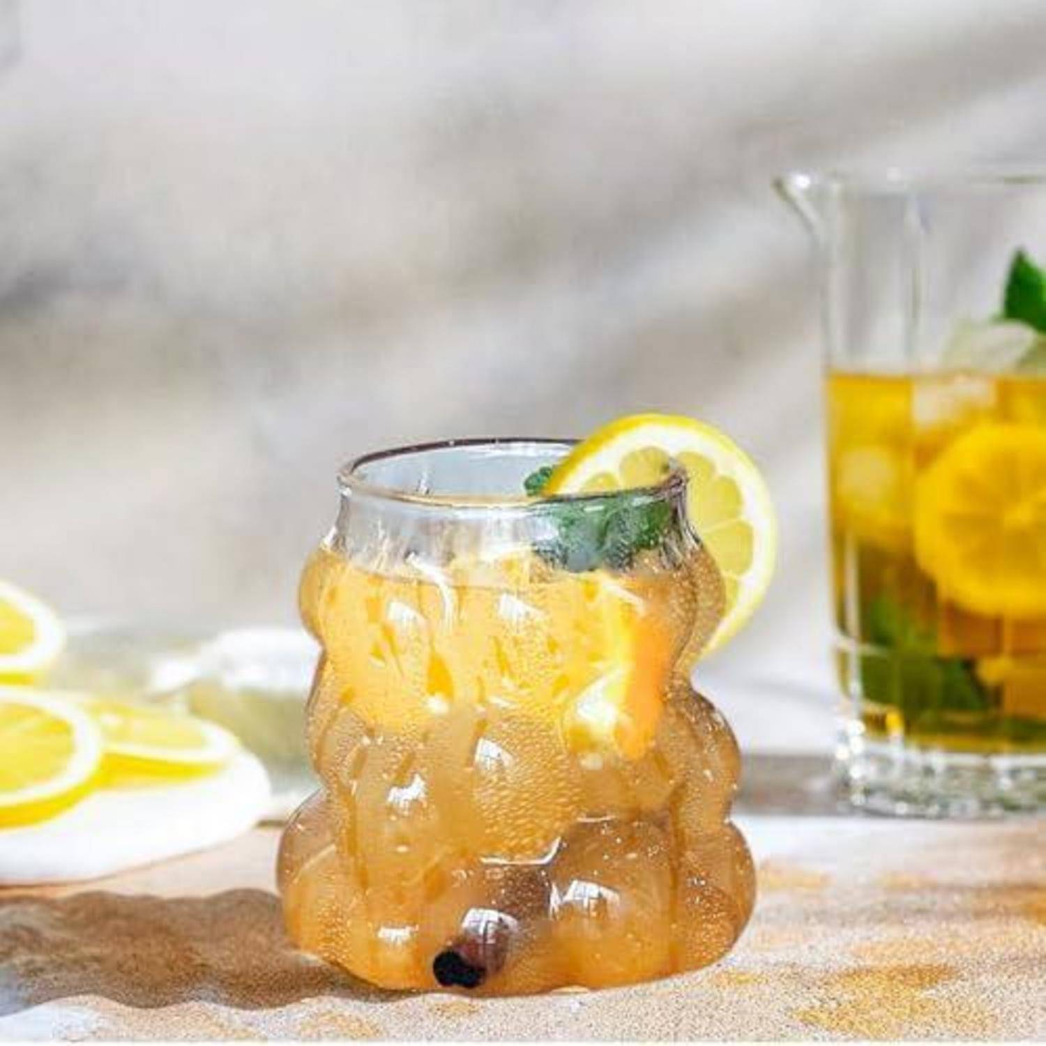Glas mit eisgekühltem Zitrusgetränk mit Zitronenscheiben und Minze, zentriert auf einem Tisch mit einem weiteren passenden Getränk im Hintergrund.
