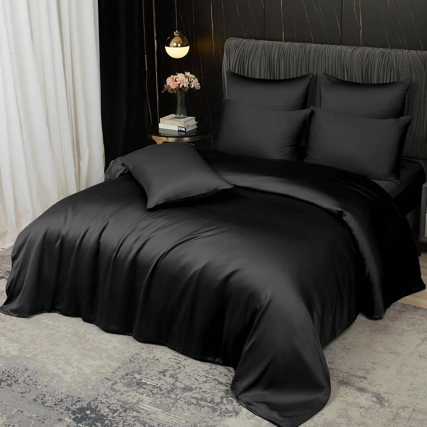 Schwarze Satin-Bettwäsche mit Kissen und einem Dekokissen auf einem ordentlich gemachten Bett in einem dunklen, eleganten Schlafzimmer.