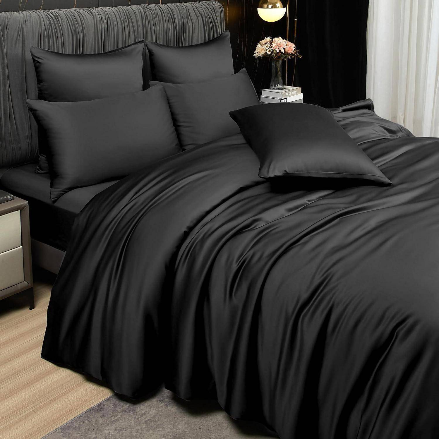 Schwarze Satin-Bettwäsche auf einem ordentlich gemachten Bett mit mehreren Kissen und einem passenden schwarzen Wurf-Kissen in einem modernen Schlafzimmer.