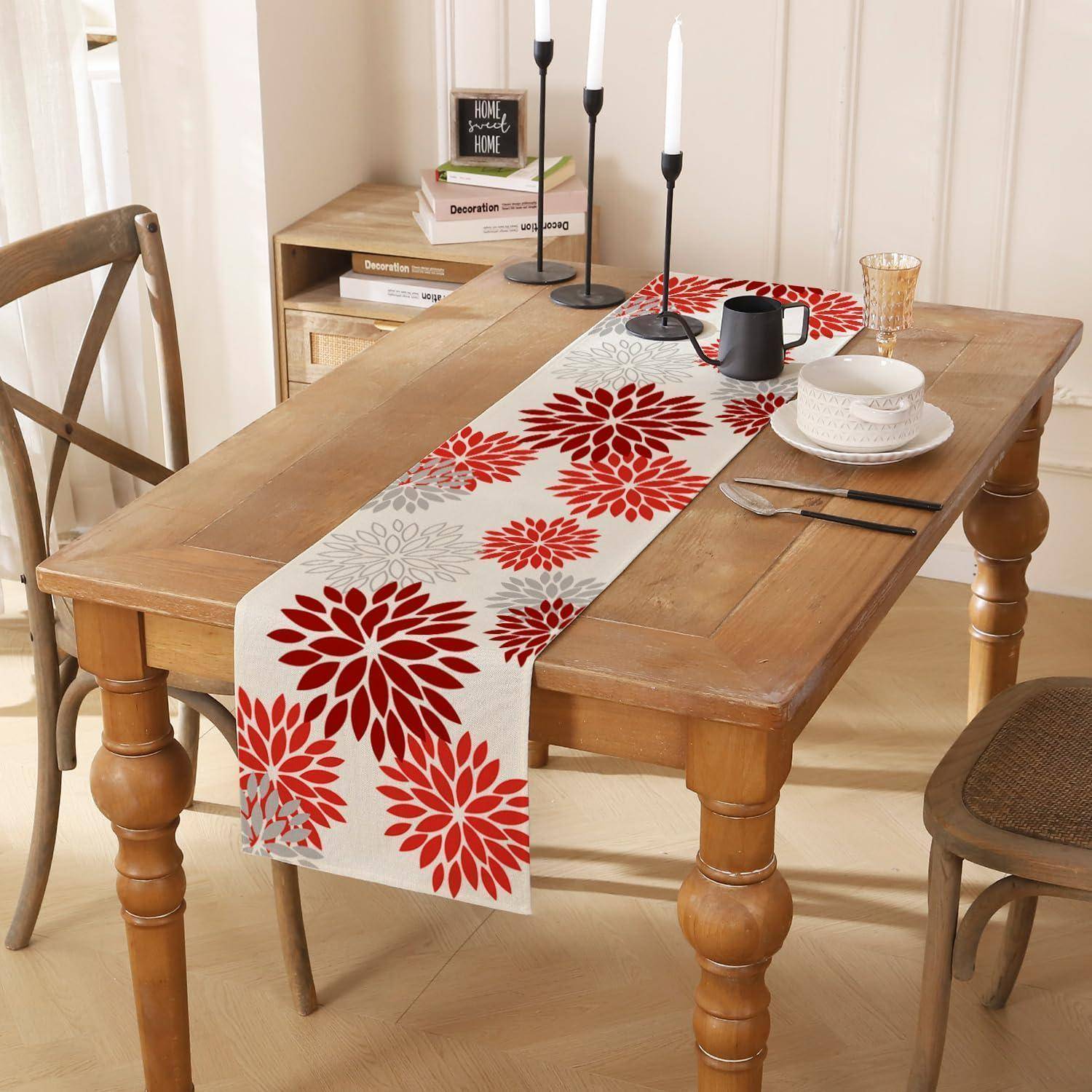 Holzesszimmertischset für ein Platzgedeck mit einem roten Blumenlaufer, Kerzen, Tassen, Tellern und Stühlen in einem hellen Raum.