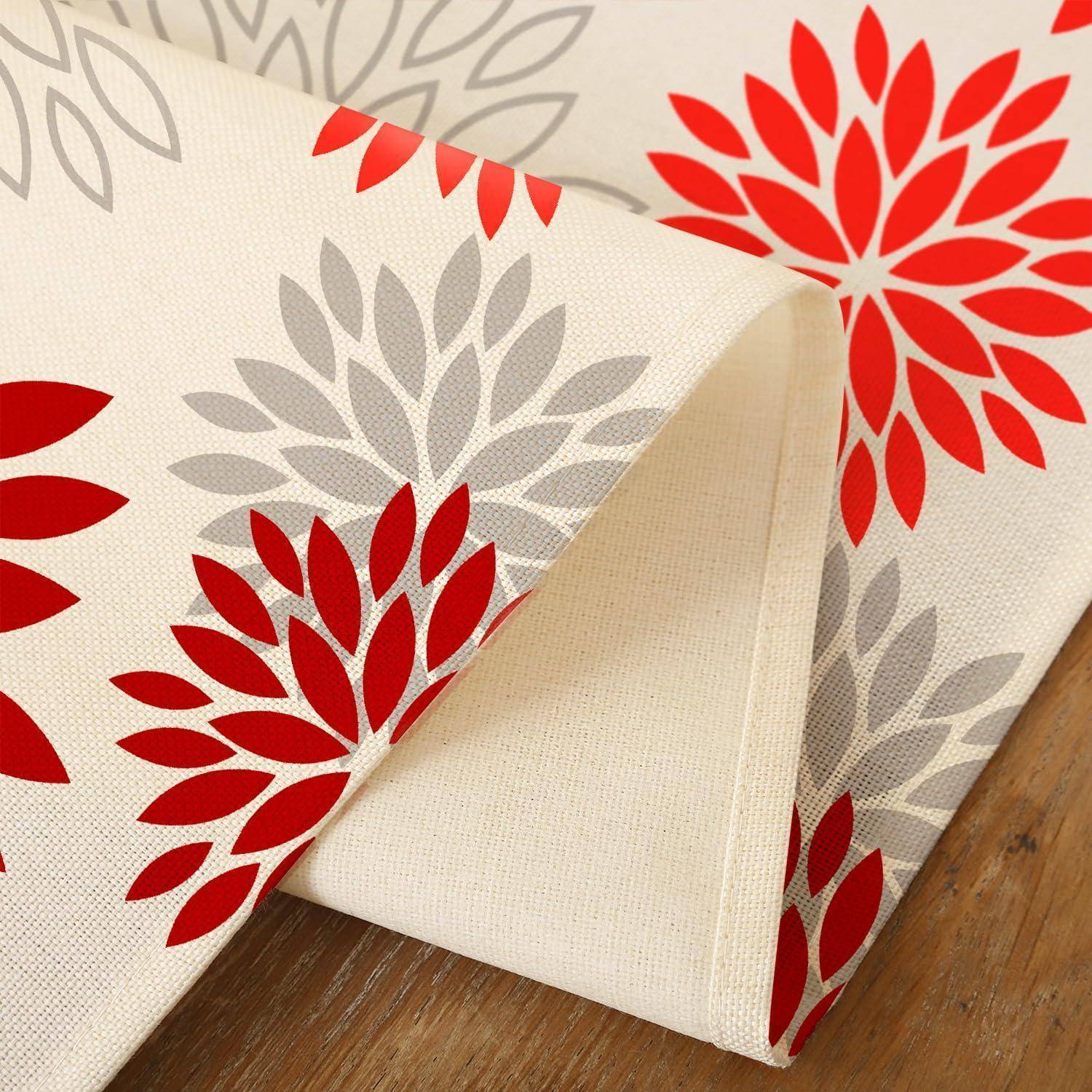 Nahaufnahme von gefalttem cremefarbenem Stoff mit rot-grauem Blatt-Blumenmuster auf einer Holzoberfläche.