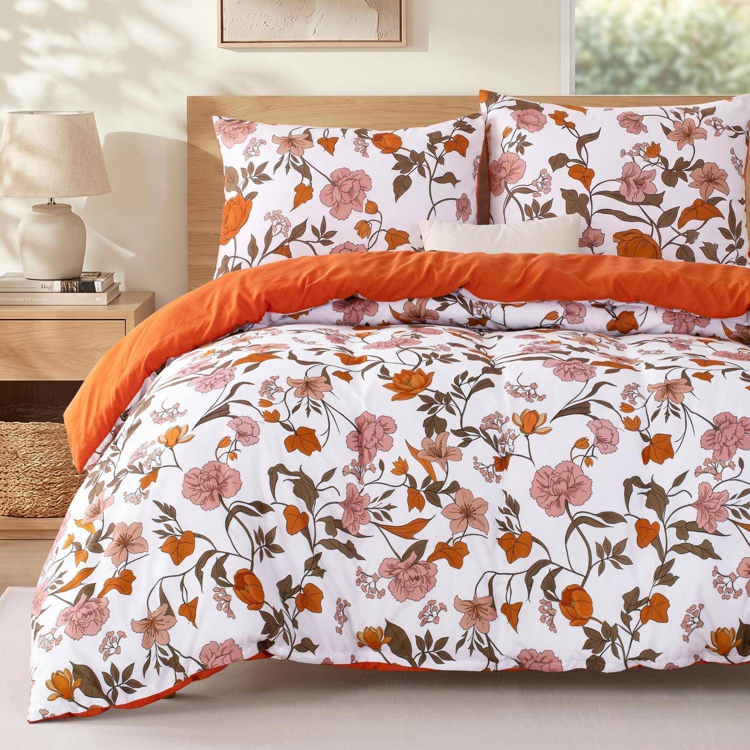 Bett mit weiß gemusterter Bettdecke und Kissen mit Blumenmuster, akzentuiert durch eine orangefarbene Wurfdecke in einem sanft beleuchteten Schlafzimmer.