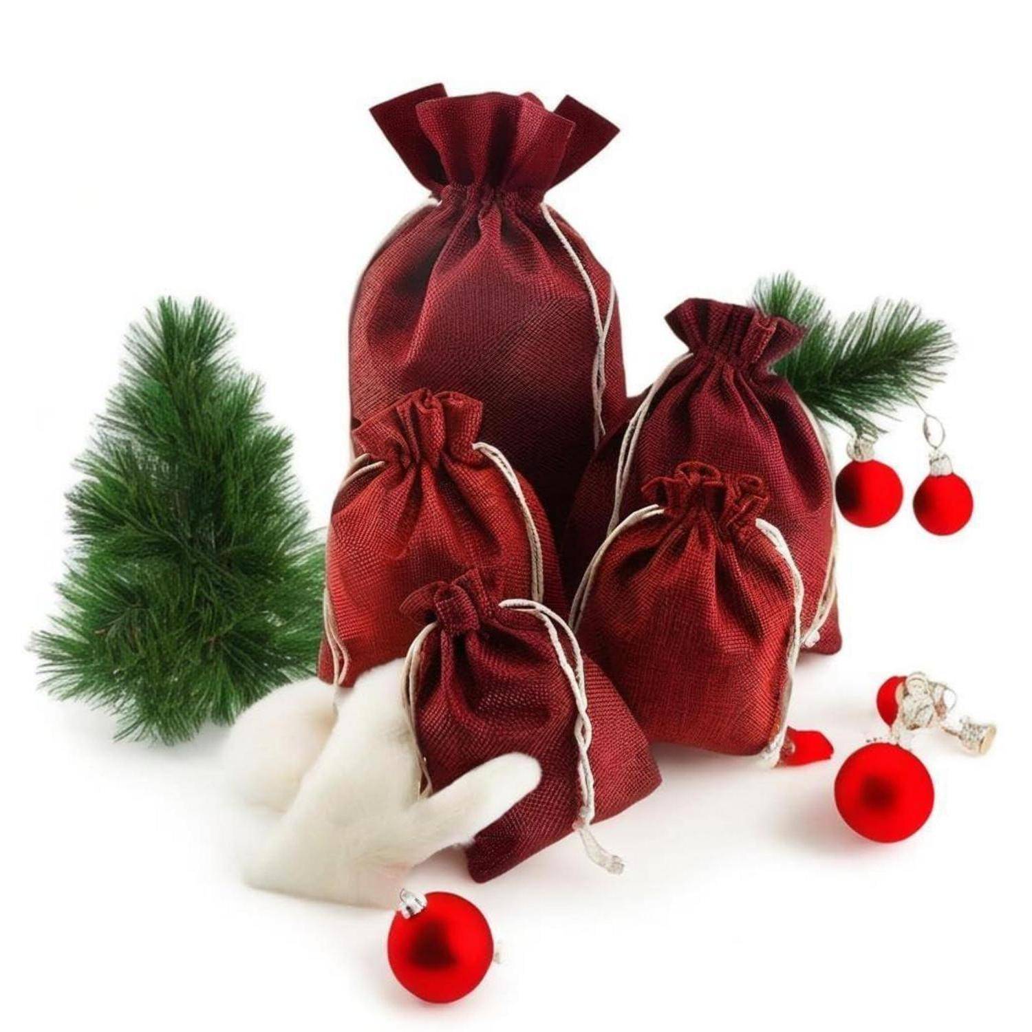 Samtverhangene Geschenktüten in Rot angeordnet mit kleinen Weihnachtskugeln, Kiefernzweigen und weißen künstlichen Pelzakzenten auf weißem Hintergrund.
