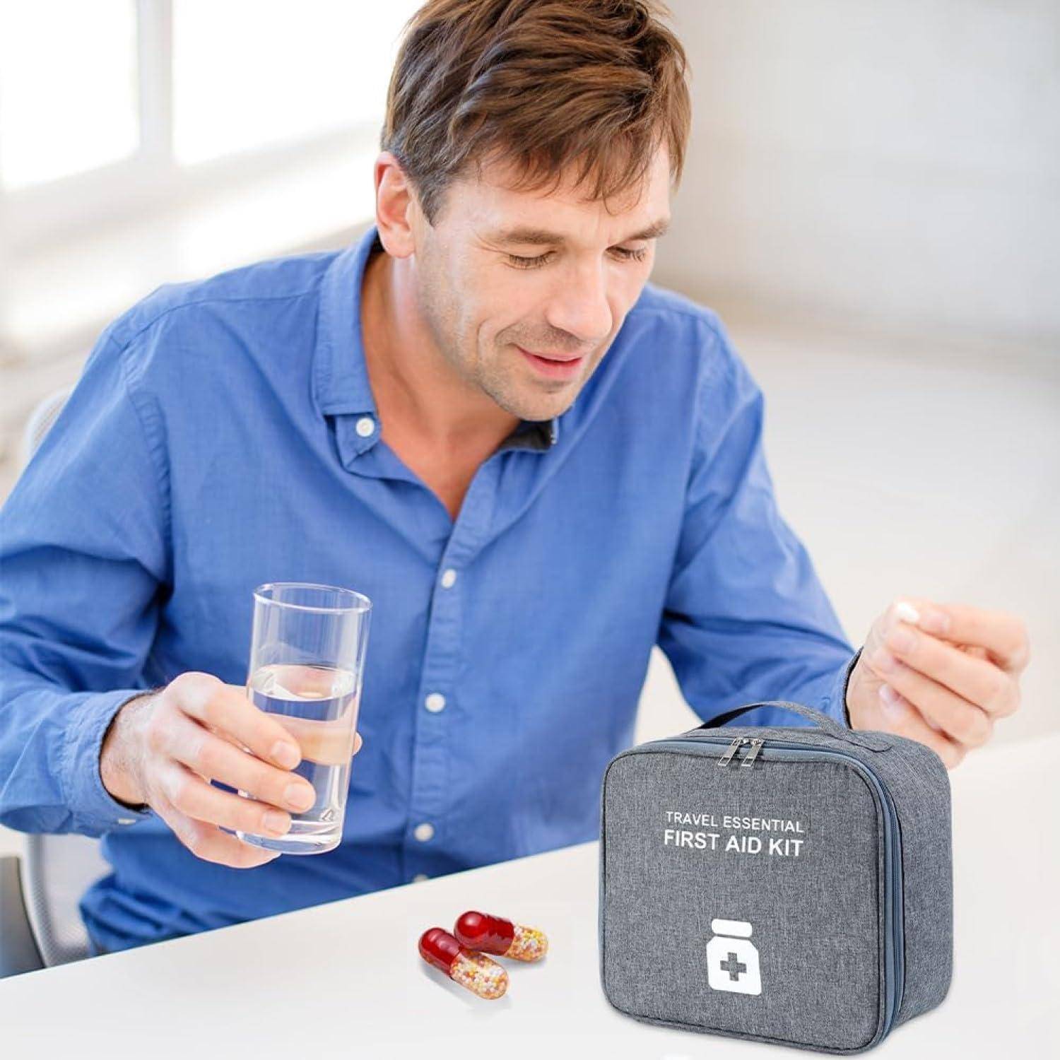 Mann, der ein Glas Wasser und eine Tablette neben einem Reise-Erste-Hilfe-Set auf einem Tisch hält.