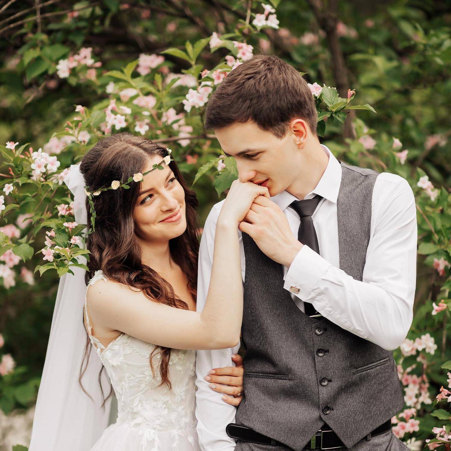 Braut und Bräutigam in Hochzeitskleidung teilen einen zärtlichen Moment im Freien inmitten blühender rosa Blumen.