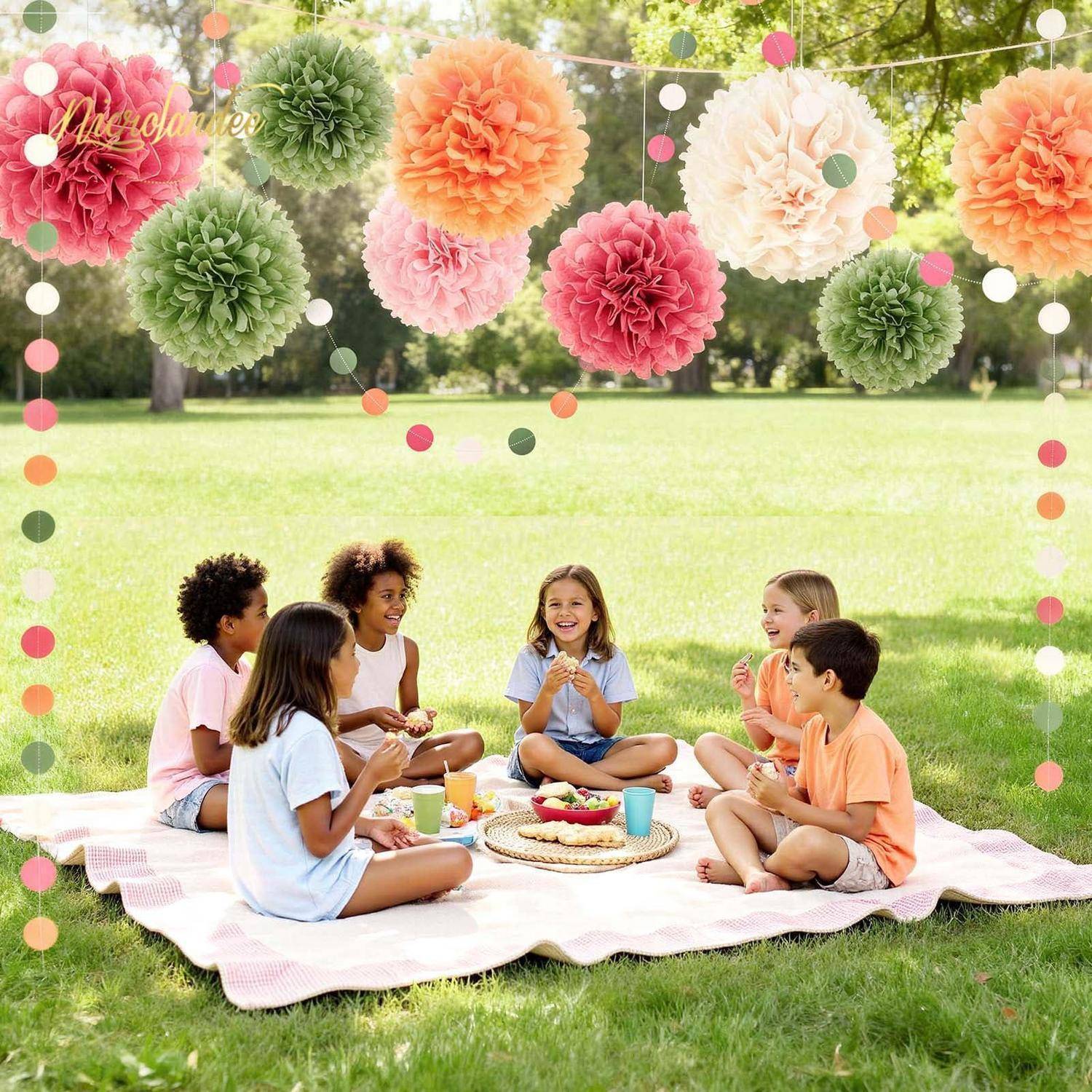 Kinder sitzen auf einer Decke und machen ein Picknick im Park, unter bunten hängenden Papierblüten und Lichterketten.