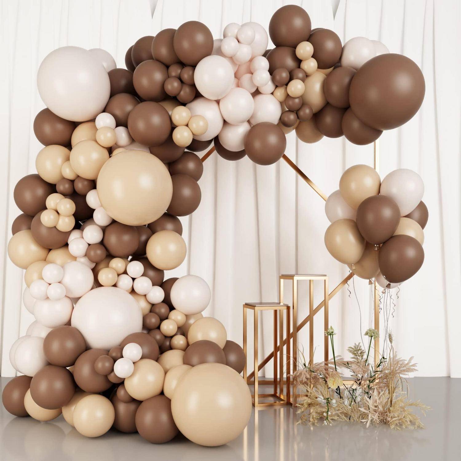 Großer brauner, beiger und weißer Ballonbogen mit passendem Balloncluster neben goldenen Ständern und getrockneter Blumendekoration in einem minimalistischen Event-Setup.